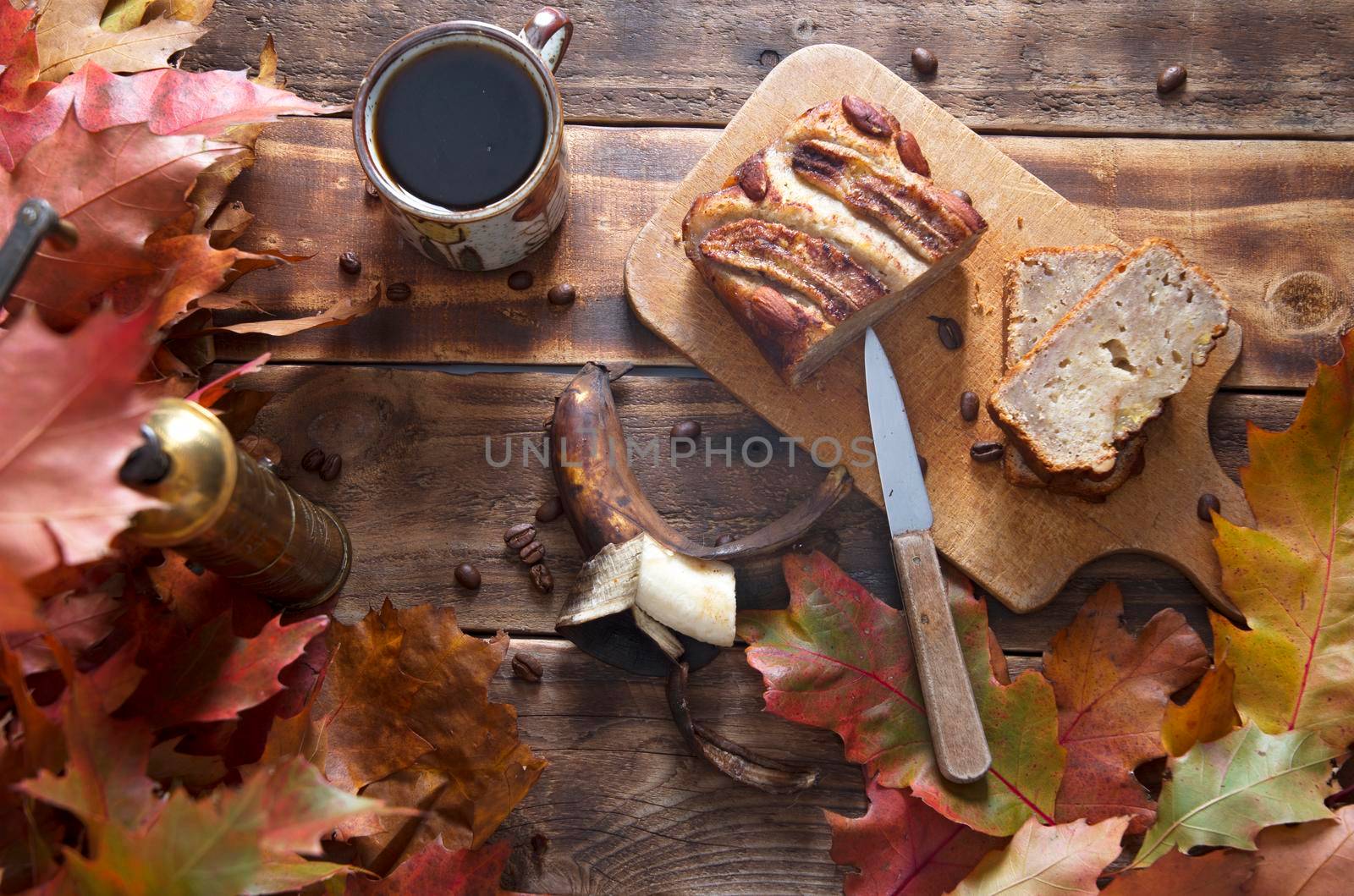 banana cake on the wooden table with orange autumn leaves, copper coffee grinder. High quality photo