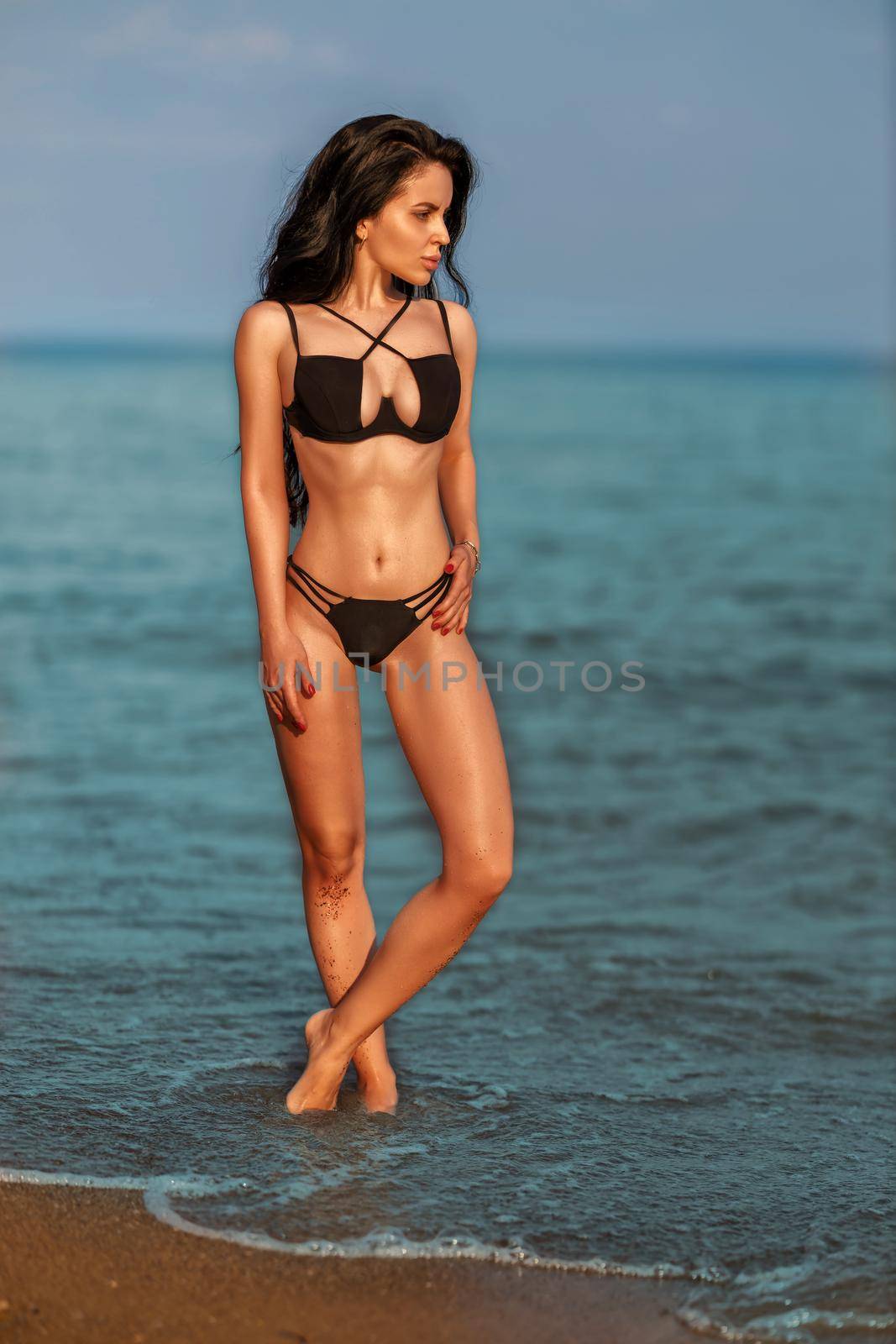 A beautiful young girl on the seashore in a black swimsuit enjoying her vacation by but_photo