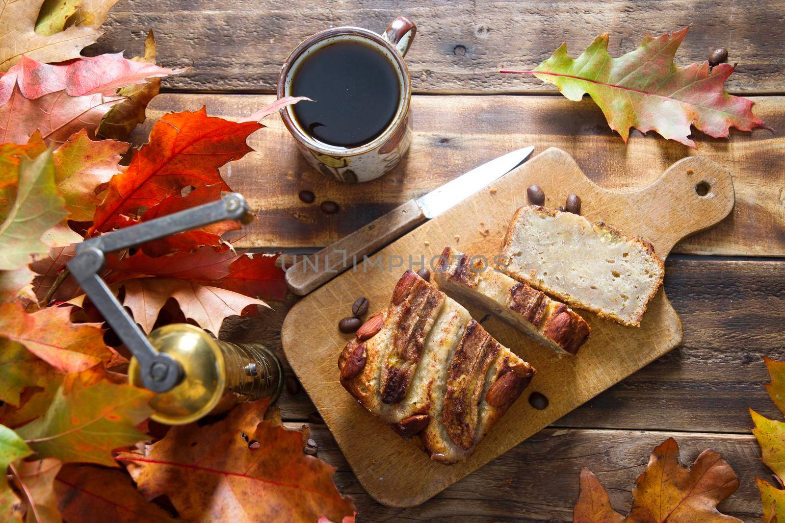banana cake on the wooden table with orange autumn leaves, copper coffee grinder. High quality photo