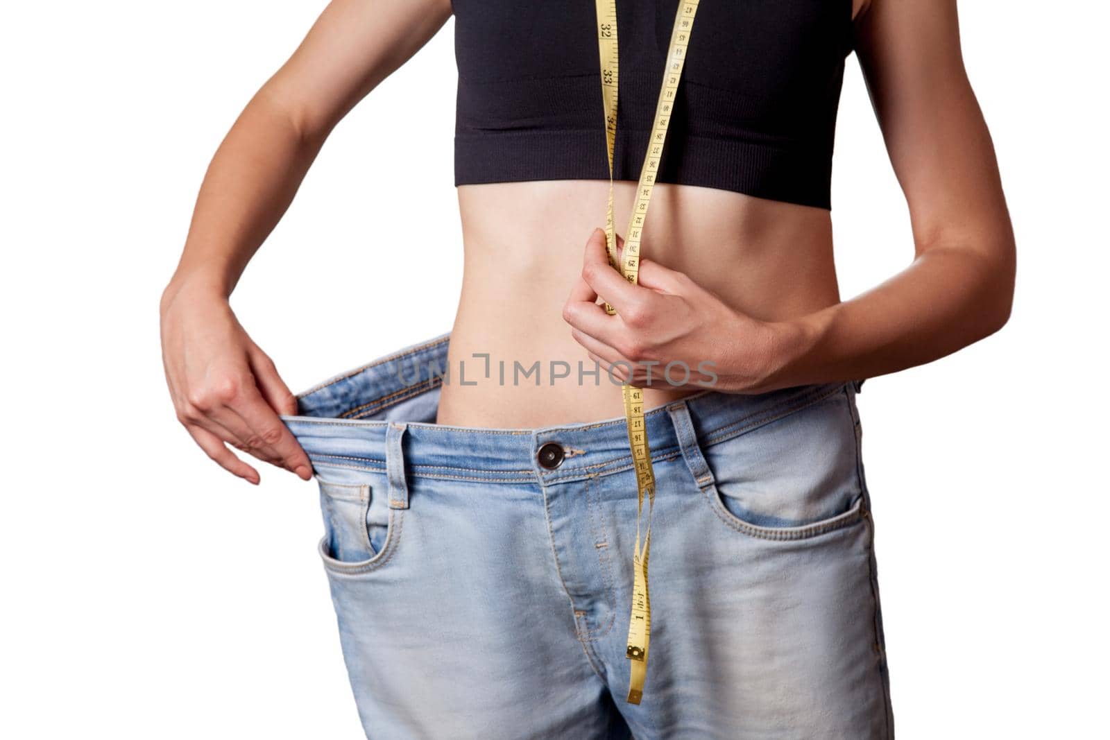 Close-up of slim waist of young woman in big jeans showing successful weight loss, isolated on white background, diet concept.