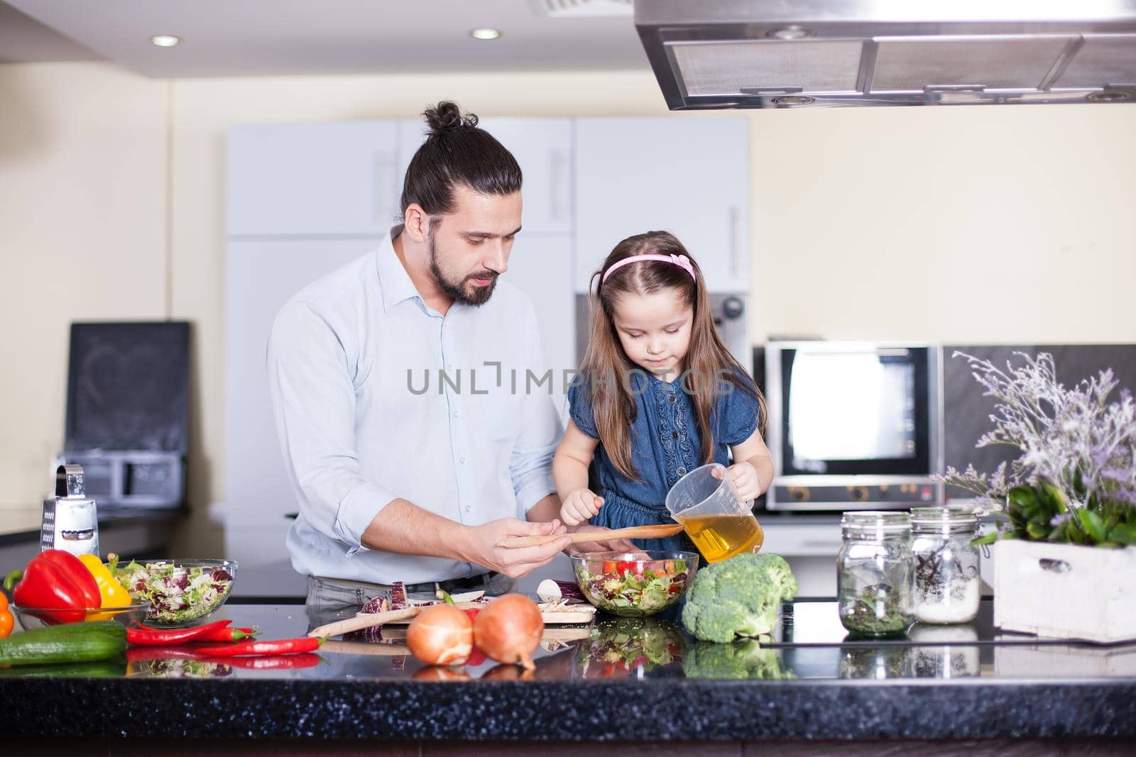 Father teaches his daughter to cook at home in the kitchen.