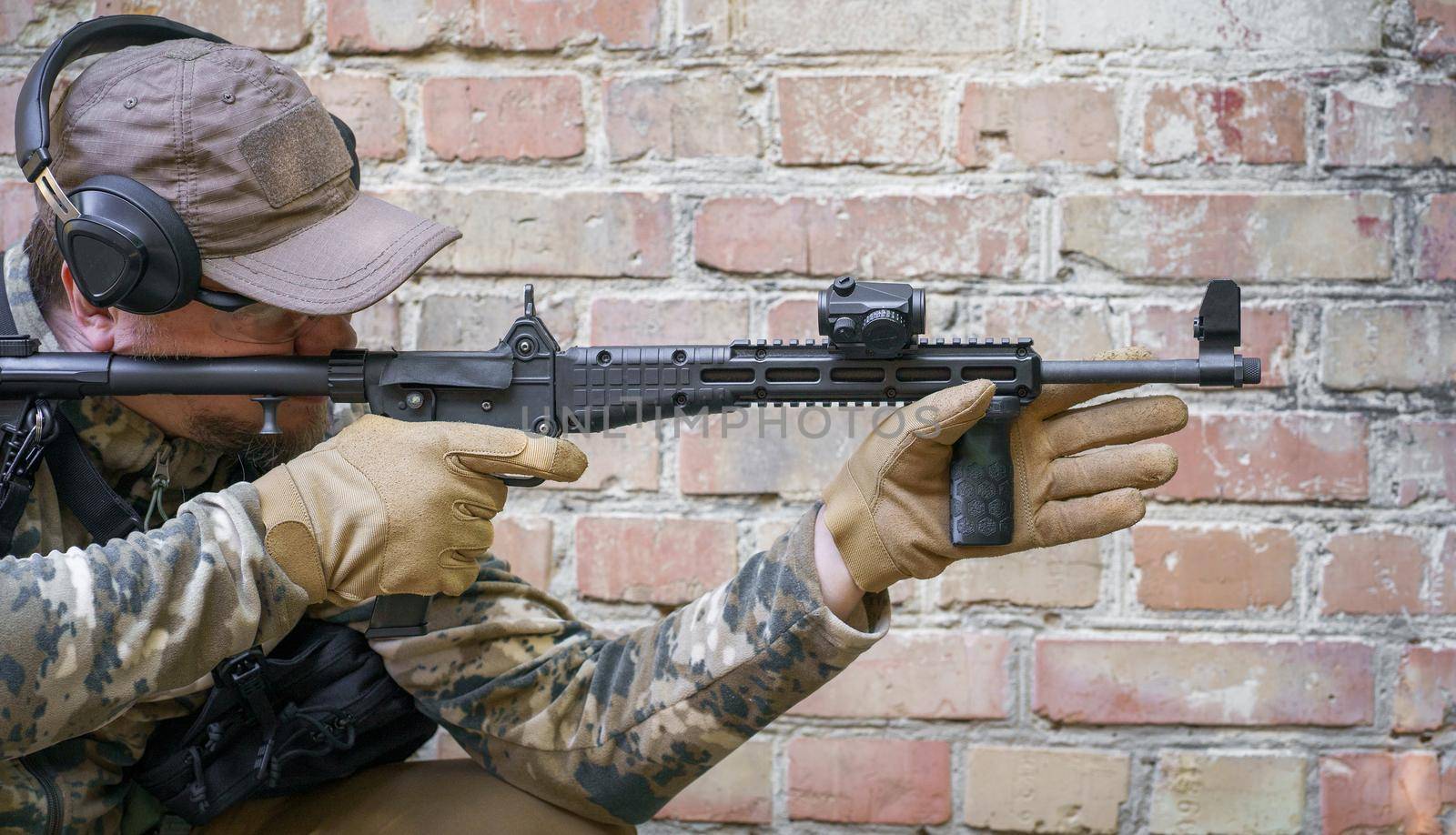 In-service training cycle for civil police troops. Man with gun standing sideways near brick wall during advanced firearms, defence tactics, use of force policy review, officer safety updates by LipikStockMedia