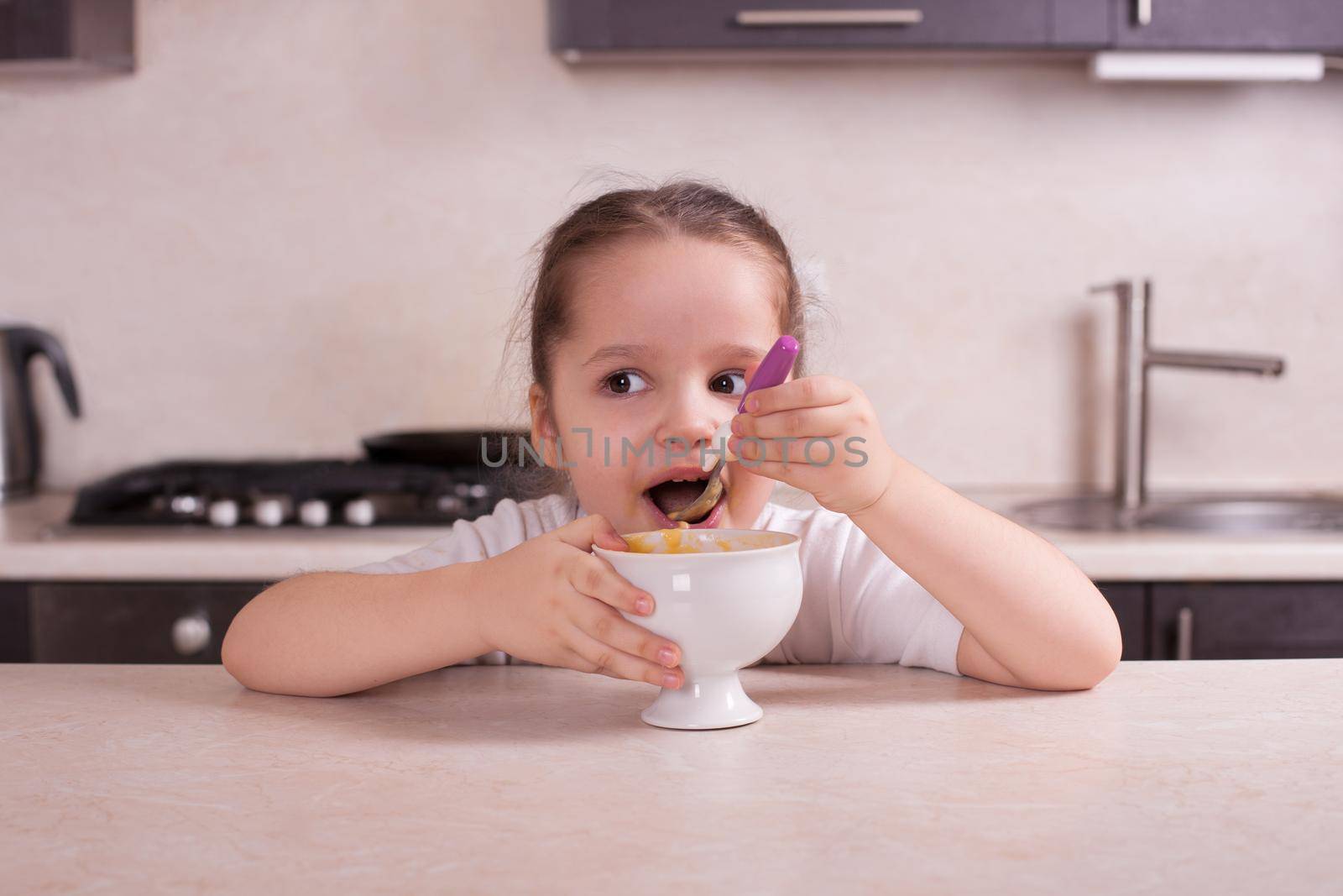 Girl eating in the kitchen soup from a pumpkin. Stock image.