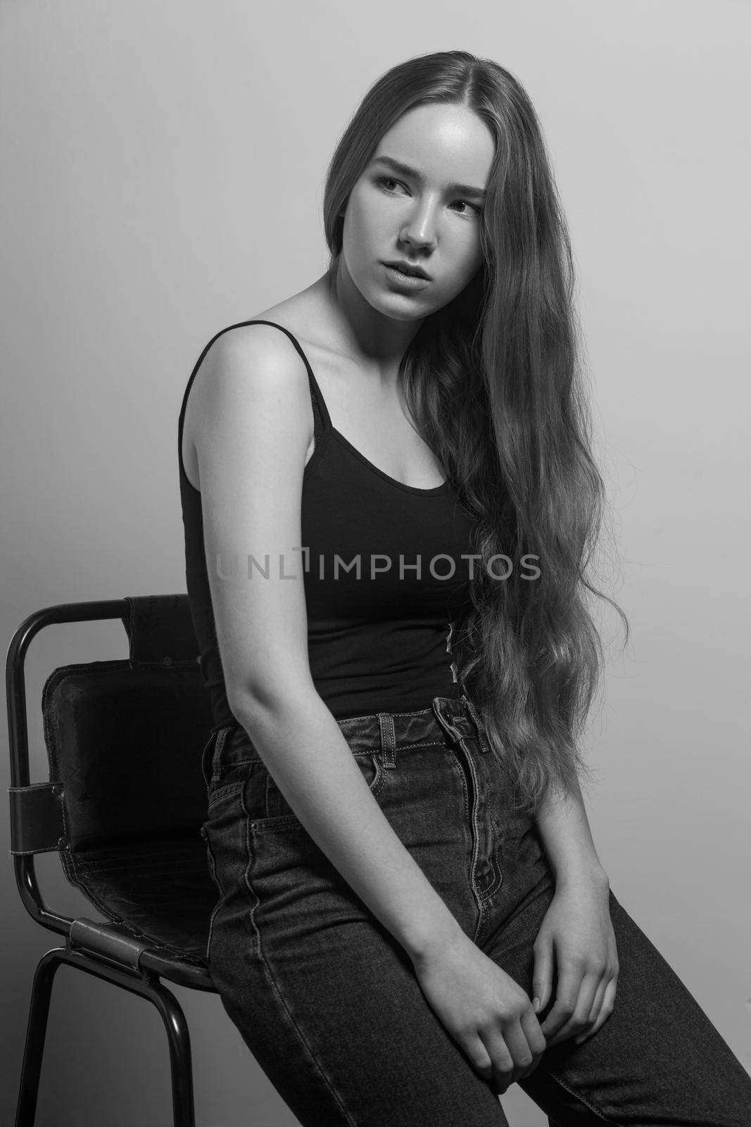 Beautiful woman sit on chair and looking away. Studio shot, isolated on gray background