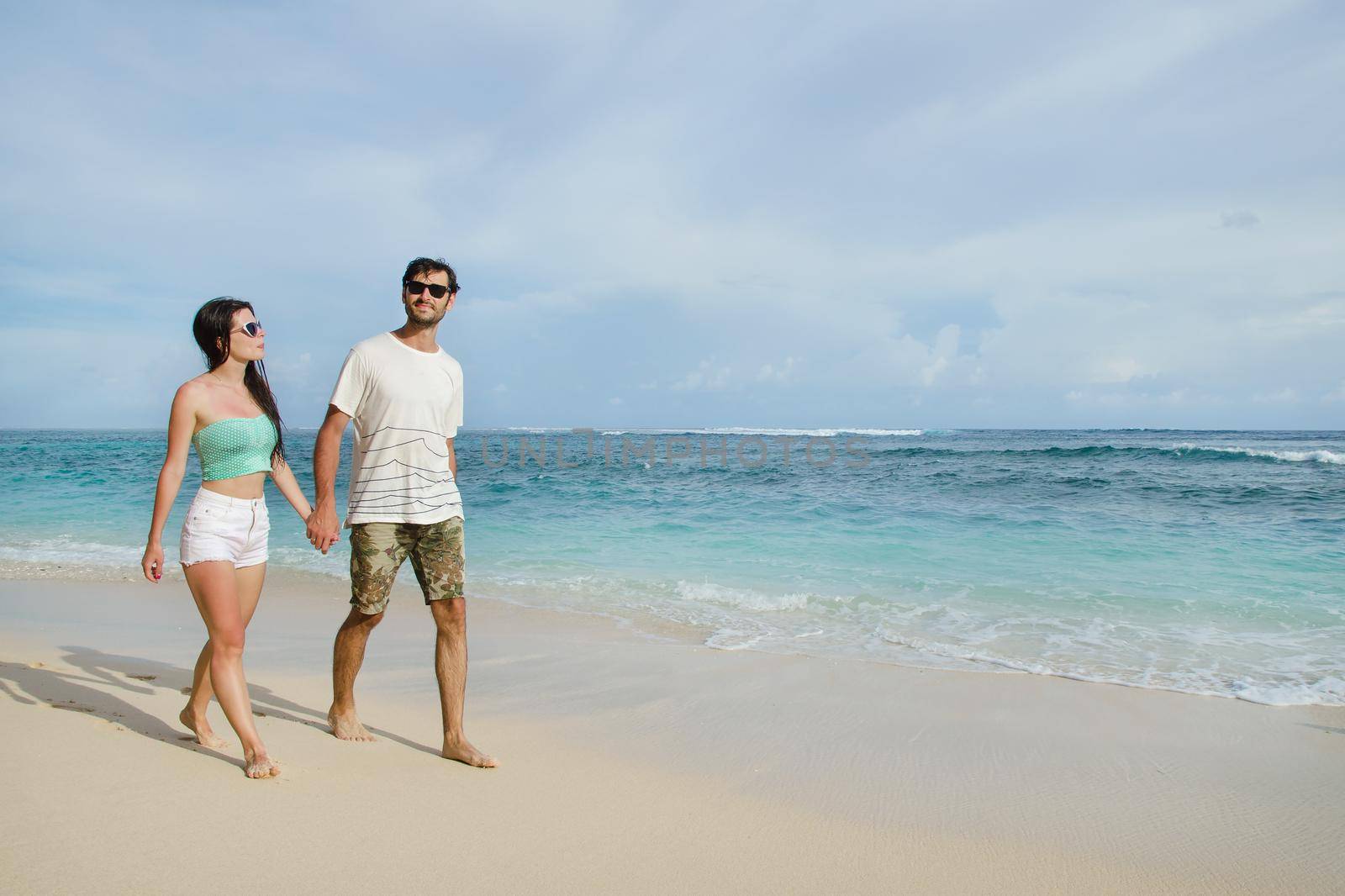 Happy young couple taking a walk holding hands on the beach. Stock image