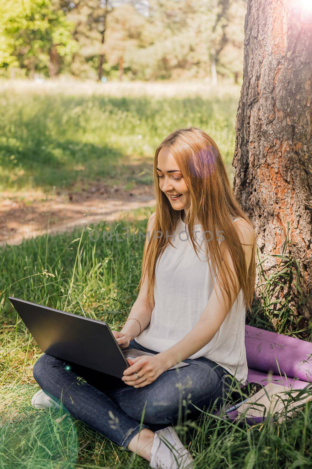 the girl sits on the grass and uses a laptop. Education, lifestyle, technology concept, outdoor learning concept by Anyatachka