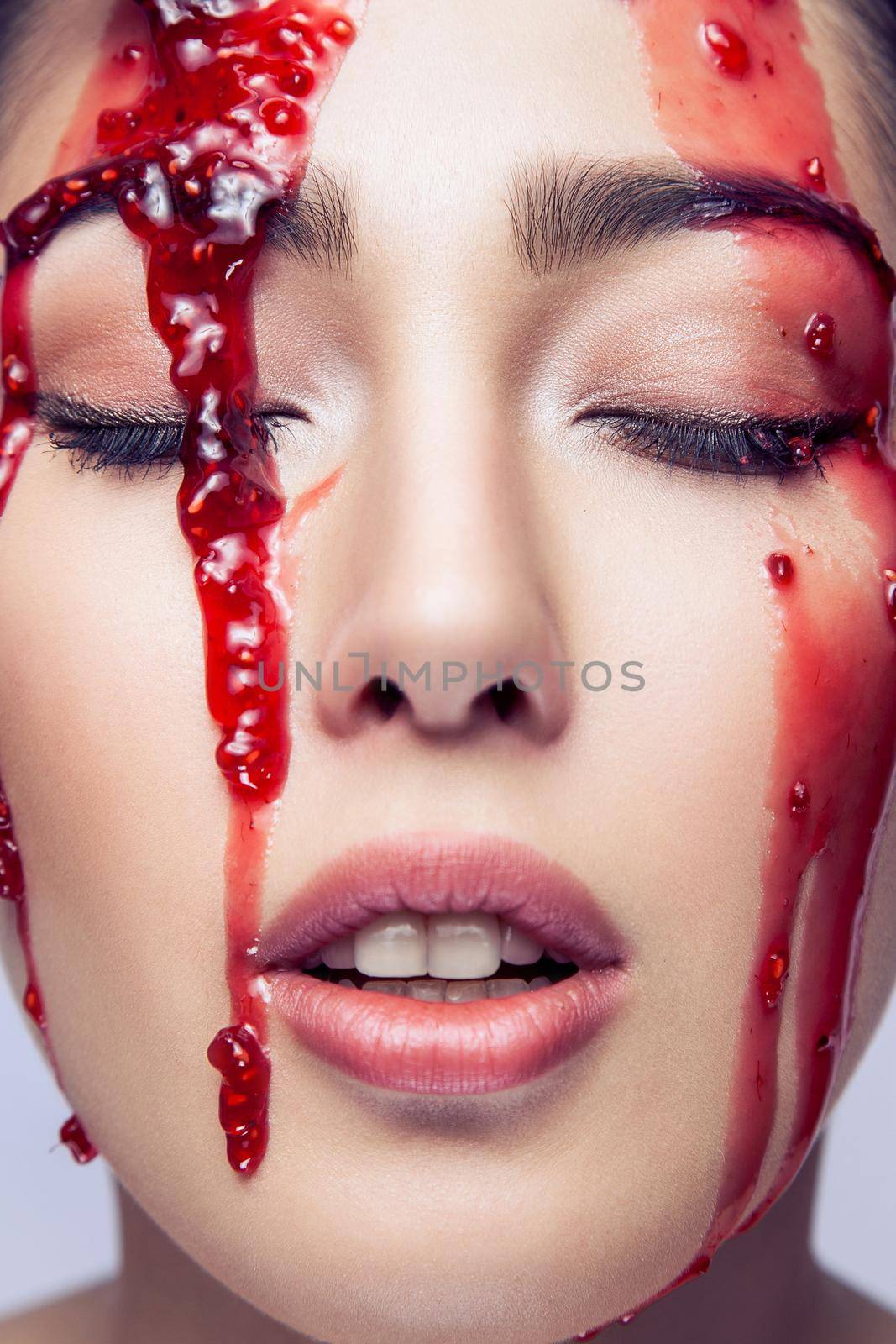 Portrait of sensual fashion model with perfect makeup. Red jam is flowing in the face. Studio shot