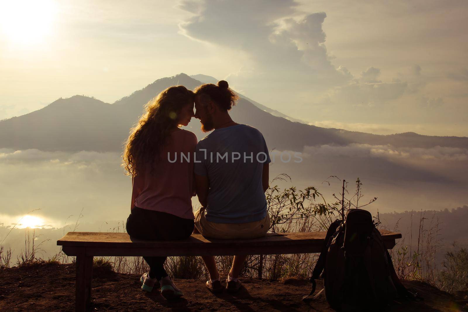 Rear view of a loving couple enjoying the sunset at the sun on top of the mountain. Stock image.