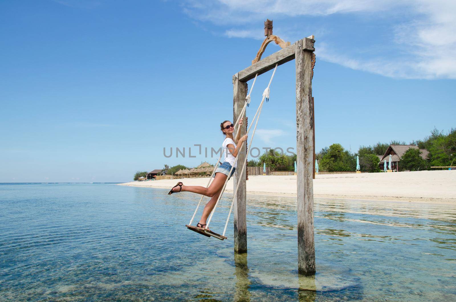 Bali, Indonesia. On the beach a young beautiful girl riding on a swing in the ocean. Stock Image