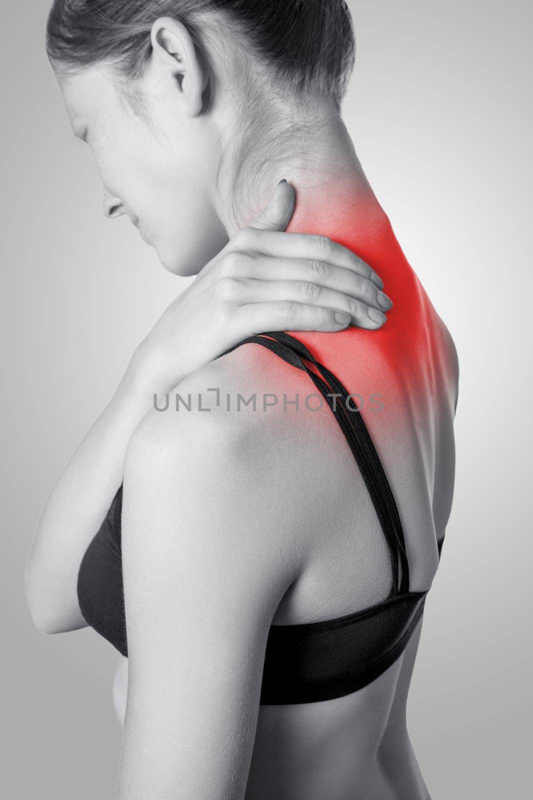Closeup view of a young woman with shoulder or neck pain on gray background. Black and white photo with red dot