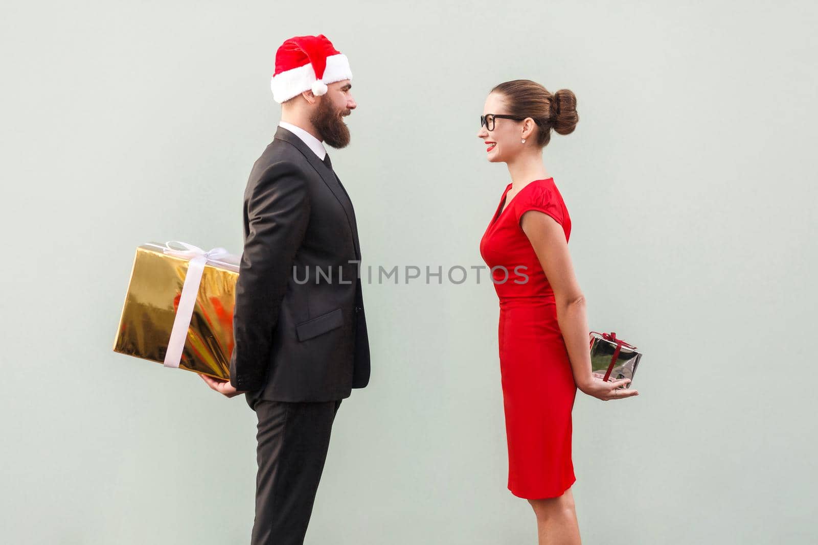 Happiness couple looking each other and holding gift box behind spine. Studio shot