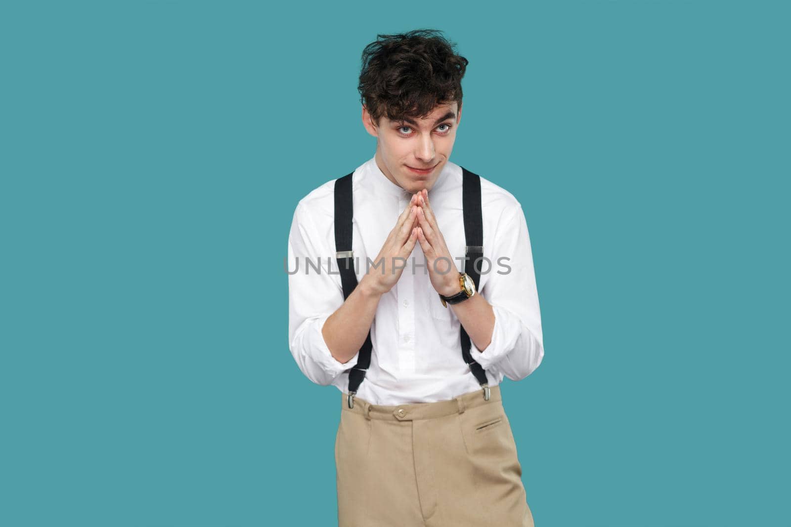 cunning funny man with plan looking at camera. Portrait of handsome hipster curly young businessman in classic casual white shirt and suspender standing. indoor studio shot isolated on blue background