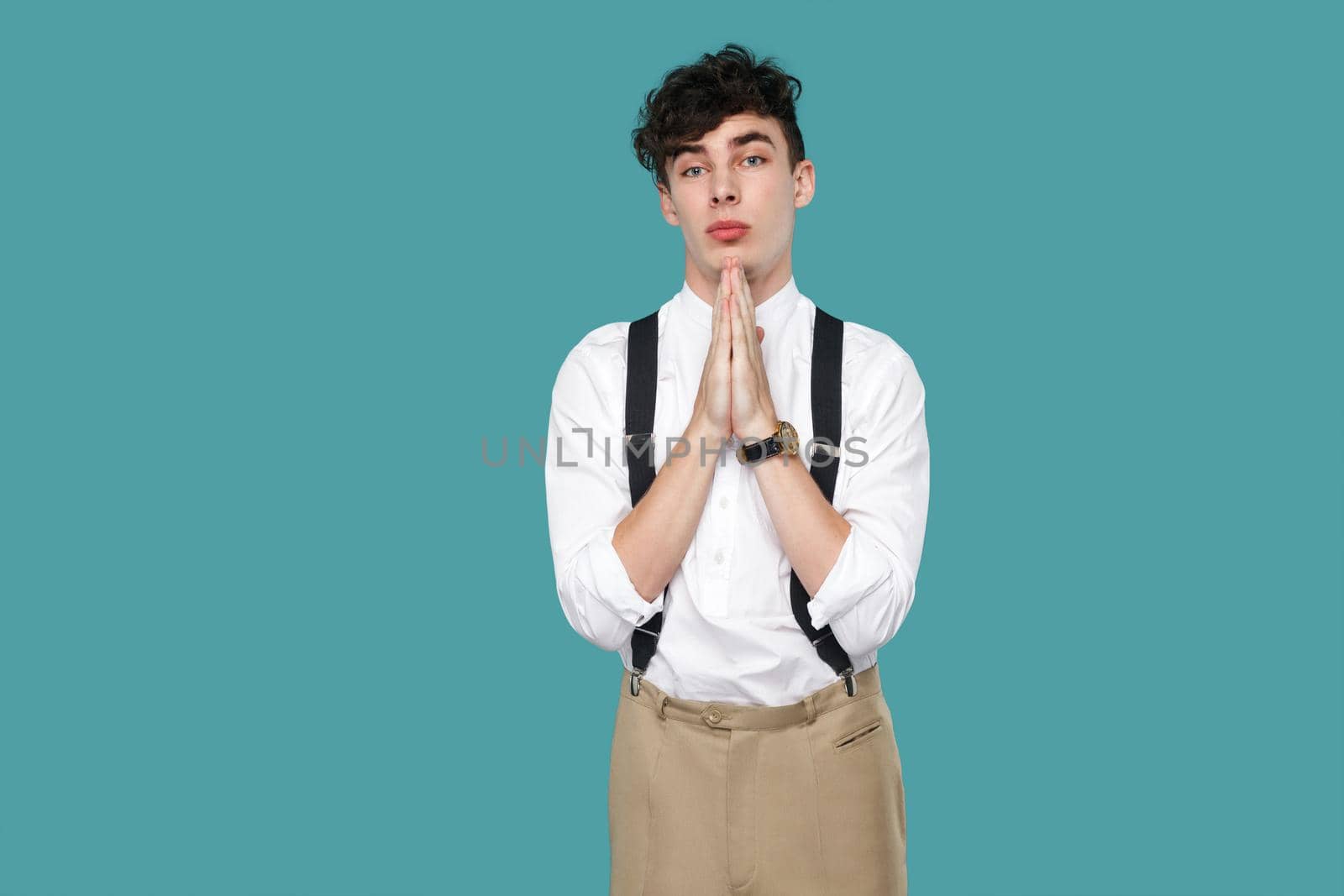 Please help me or forgive. hopeful man looking at camera. Portrait of handsome hipster curly young businessman in classic casual white shirt and suspender. studio shot isolated on blue background.