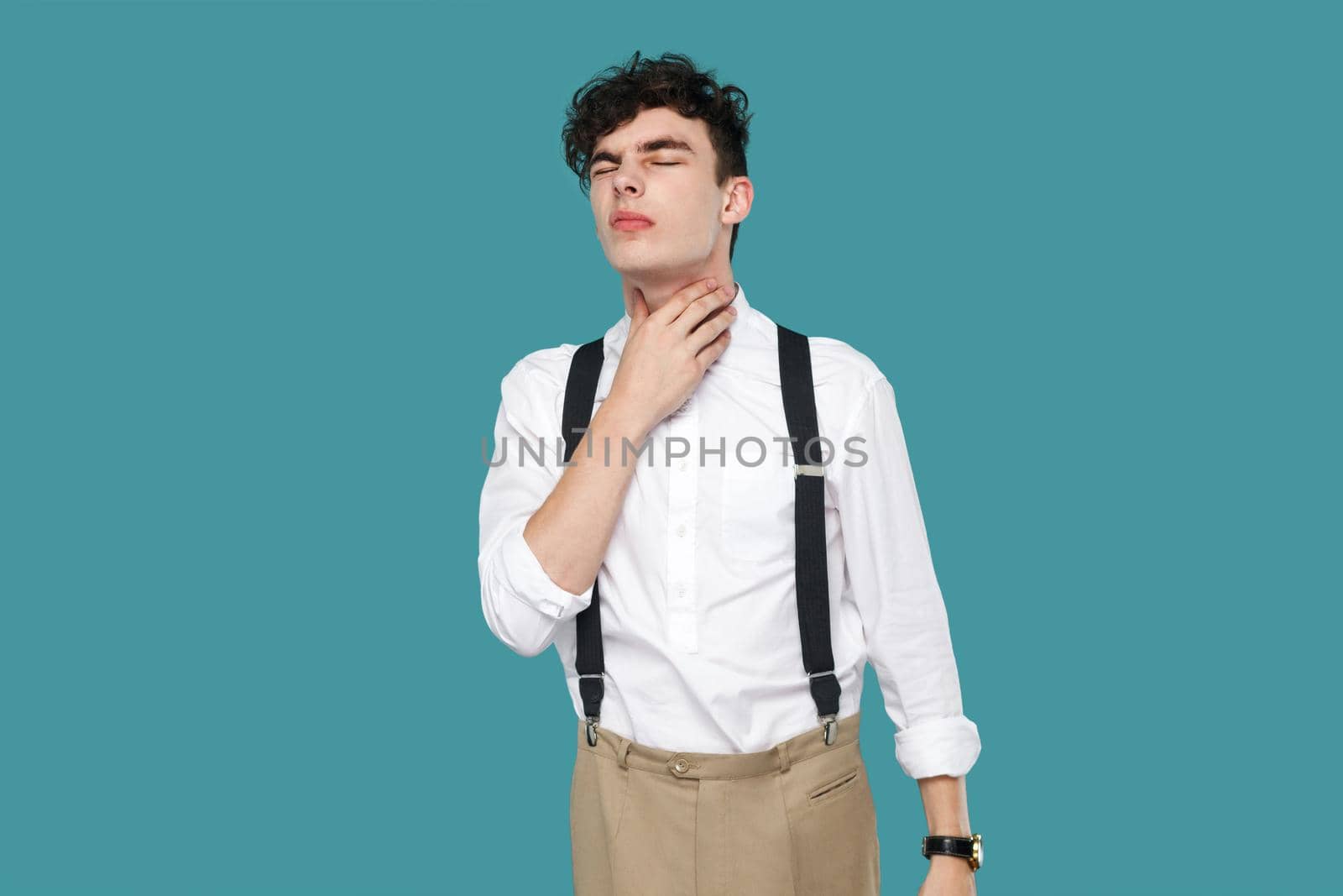 Throat pain. man holding his painful neck and feeling bad. Portrait of handsome hipster young businessman in classic casual white shirt and suspender. indoor studio shot isolated on blue background.