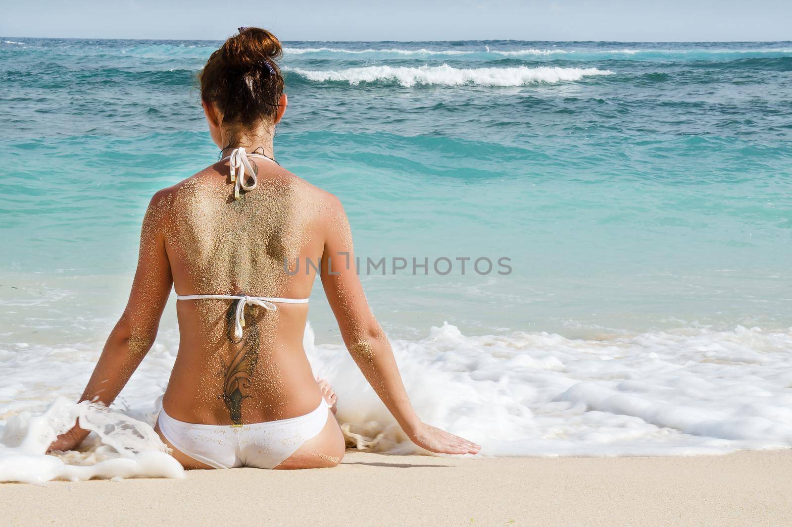Tanned young girl sitting on the beach - Stock image by Jyliana