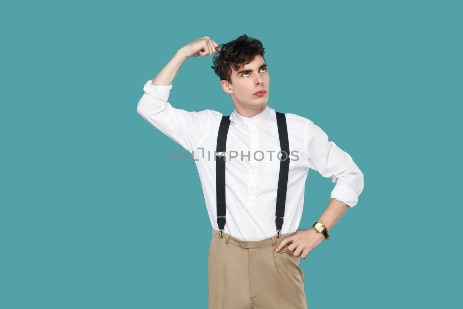 Confused man looking away and thinking. Portrait of handsome hipster curly young businessman in classic casual white shirt and suspender standing. indoor studio shot isolated on blue background.