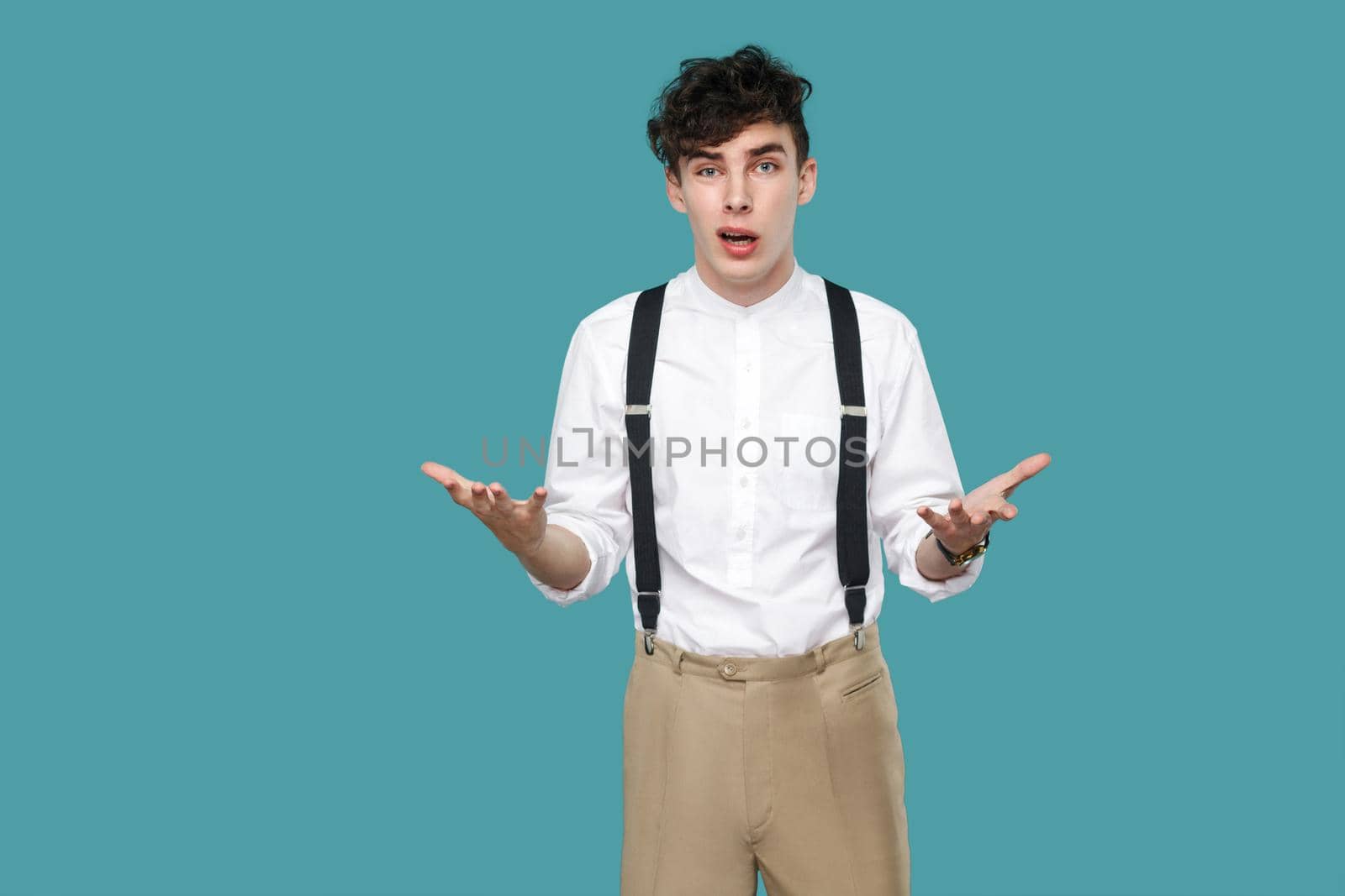 What do you want? man asking and looking at camera. Portrait of handsome hipster curly young businessman in classic casual white shirt and suspender standing. studio shot isolated on blue background.