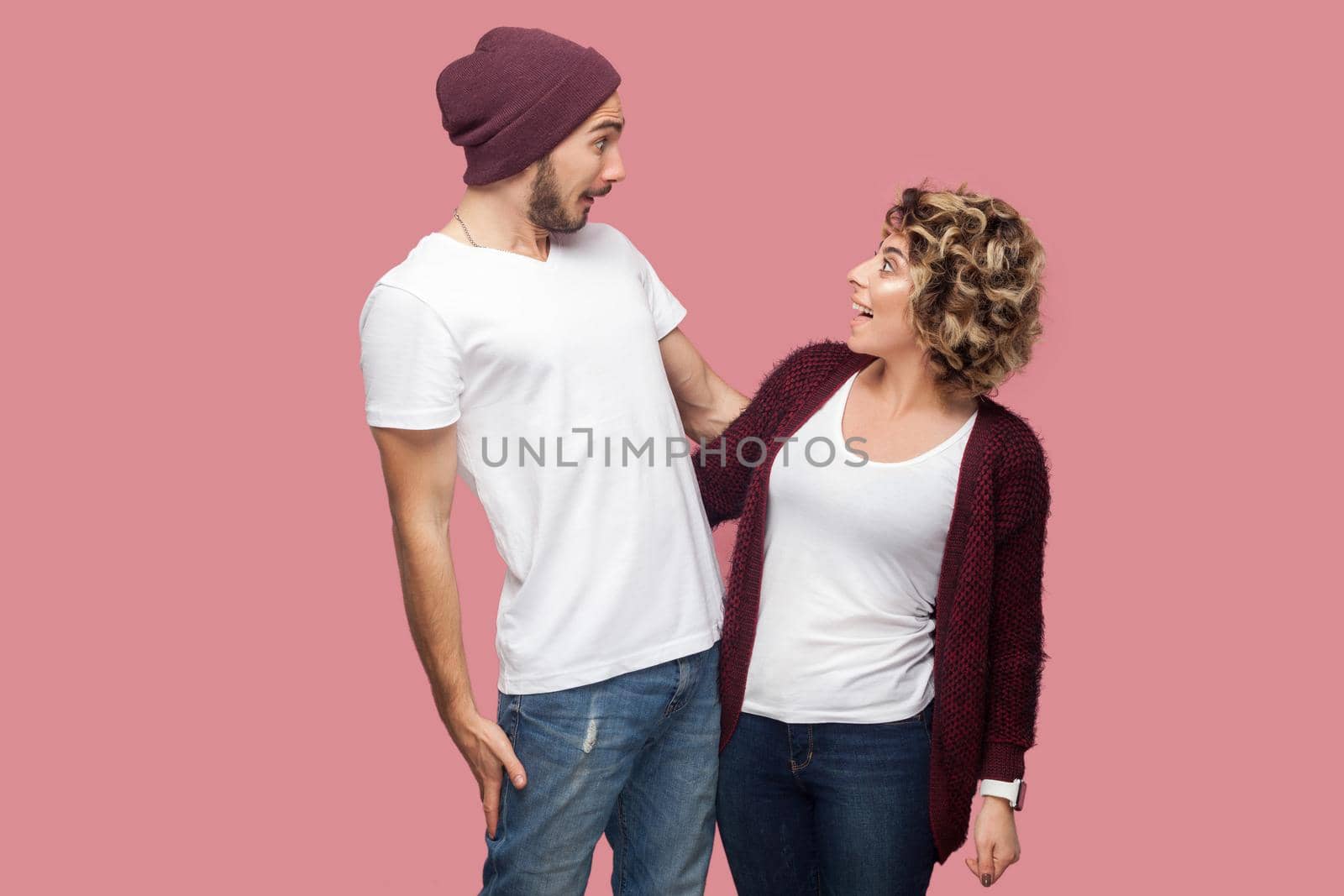No way. Portrait of excited couple of friends in casual style standing and looking to each other with amazing faces, big eyes and toothy smile. Isolated, indoor, studio shot, pink background