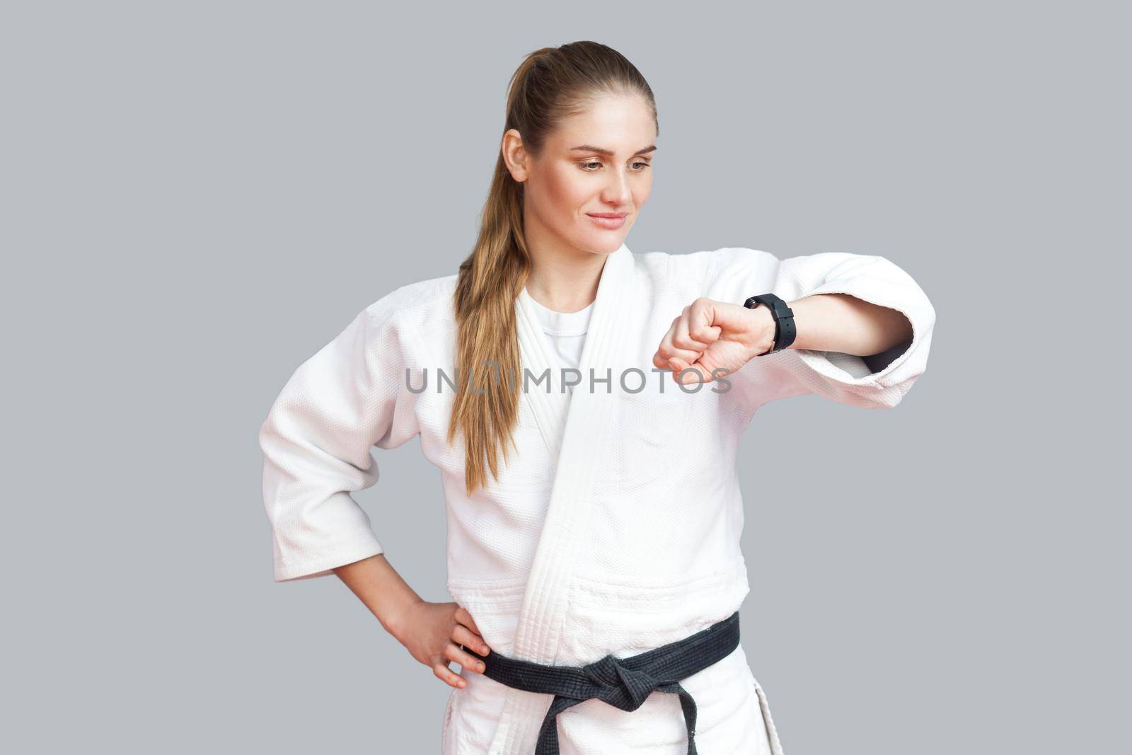 Burning calories. Athletic satisfied young blonde woman looking at smart watch counting burned calories during workout training, using fitness bracelet. Indoor studio shot, isolated on grey background