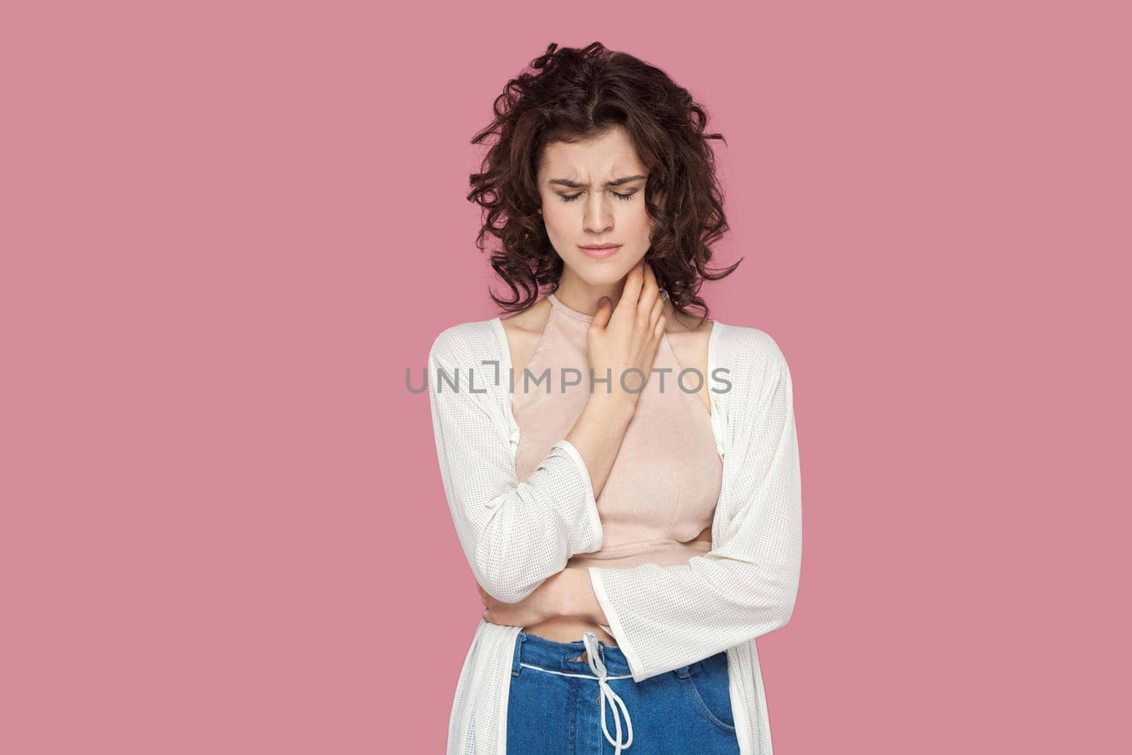 Portrait of depressed beautiful brunette young woman with curly hairstyle in casual style standing, holding her head down and crying. expression, emotion indoor studio shot isolated on pink background