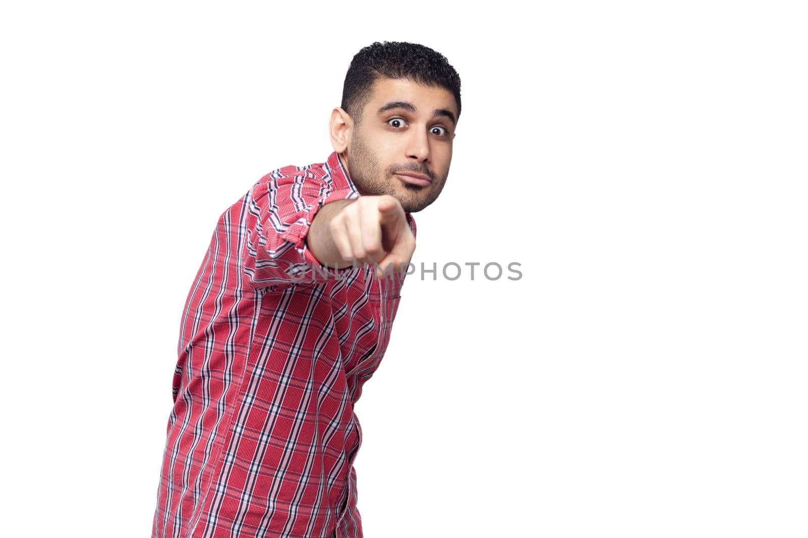 Hey you. Portrait of shocked handsome bearded young businessman in red checkered shirt standing pointing and looking at camera with big eyes. indoor studio shot, isolated on white background.