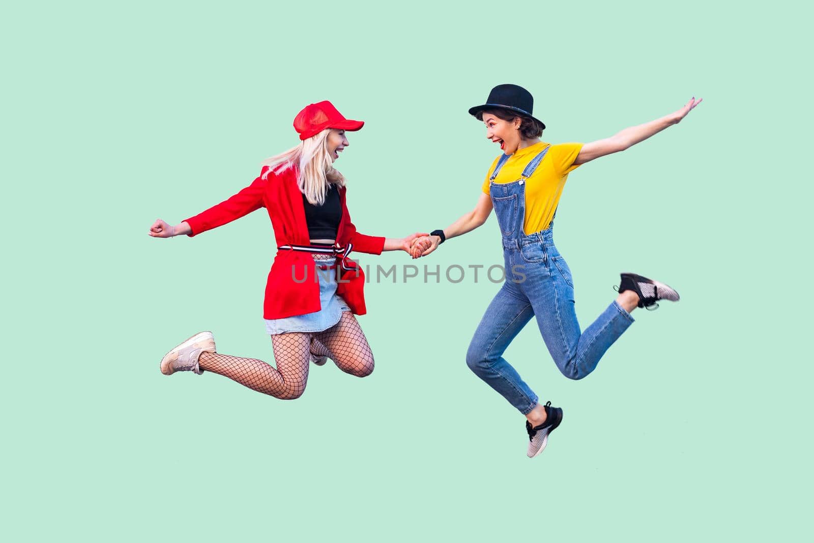 Emotional girls in casual style standing together and have fun near light green background by Khosro1