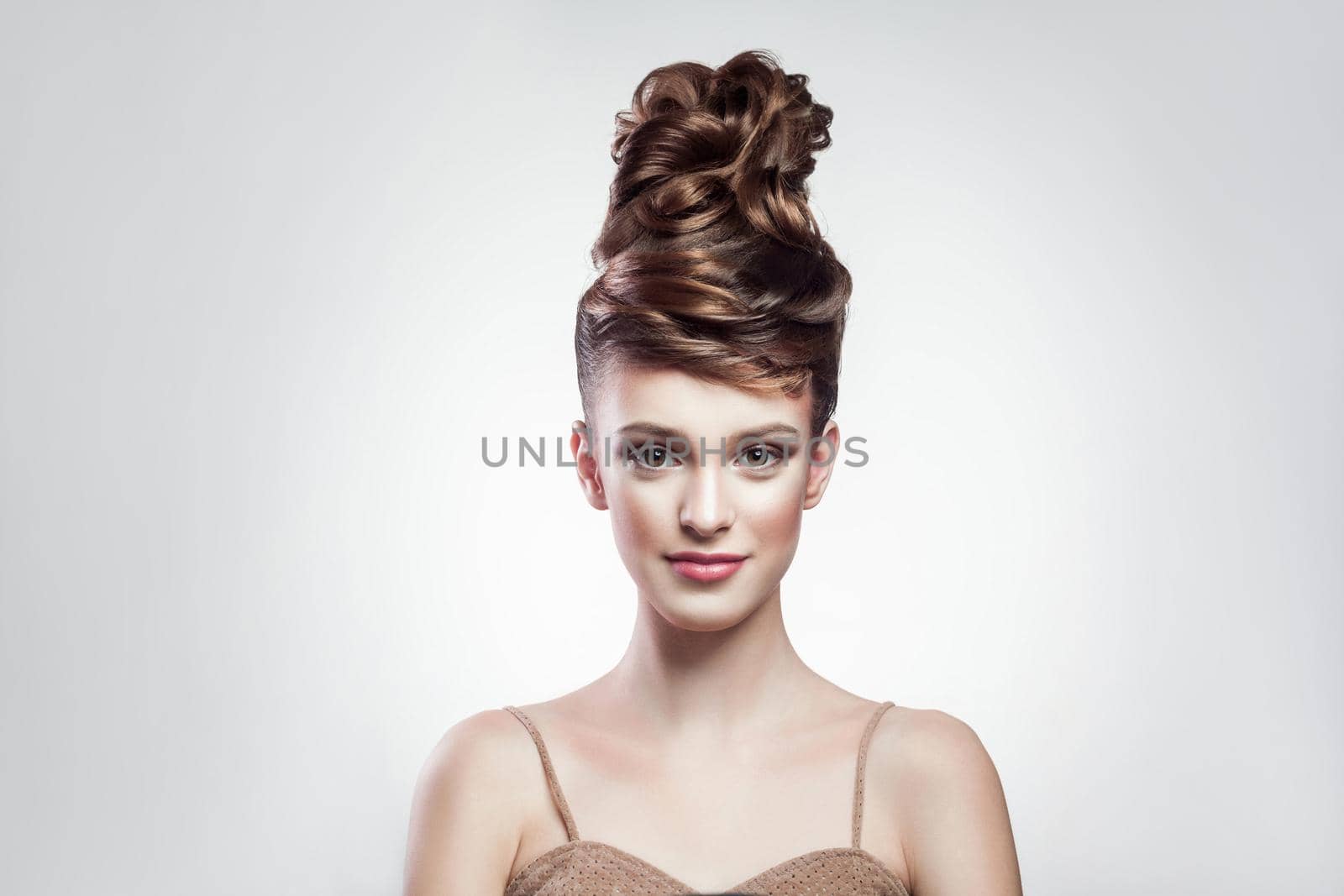 portrait of attractive brunette woman with stylish hairdo and makeup looking at camera with smimle on isolated grey background. indoor, studio shot on copy space.