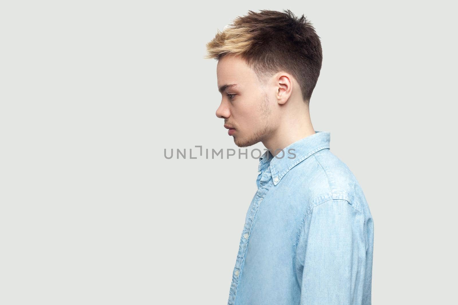 Profile side view portrait of calm serious handsome young man in light blue shirt standing and looking forward with serious face. indoor studio shot on grey background copy space.
