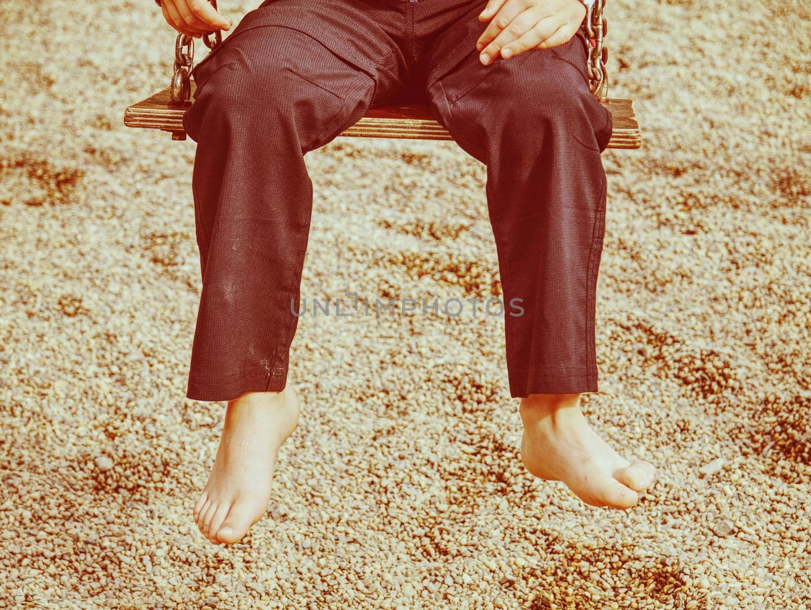 Kid sitting with feet against a sand in summer playground, concept for family