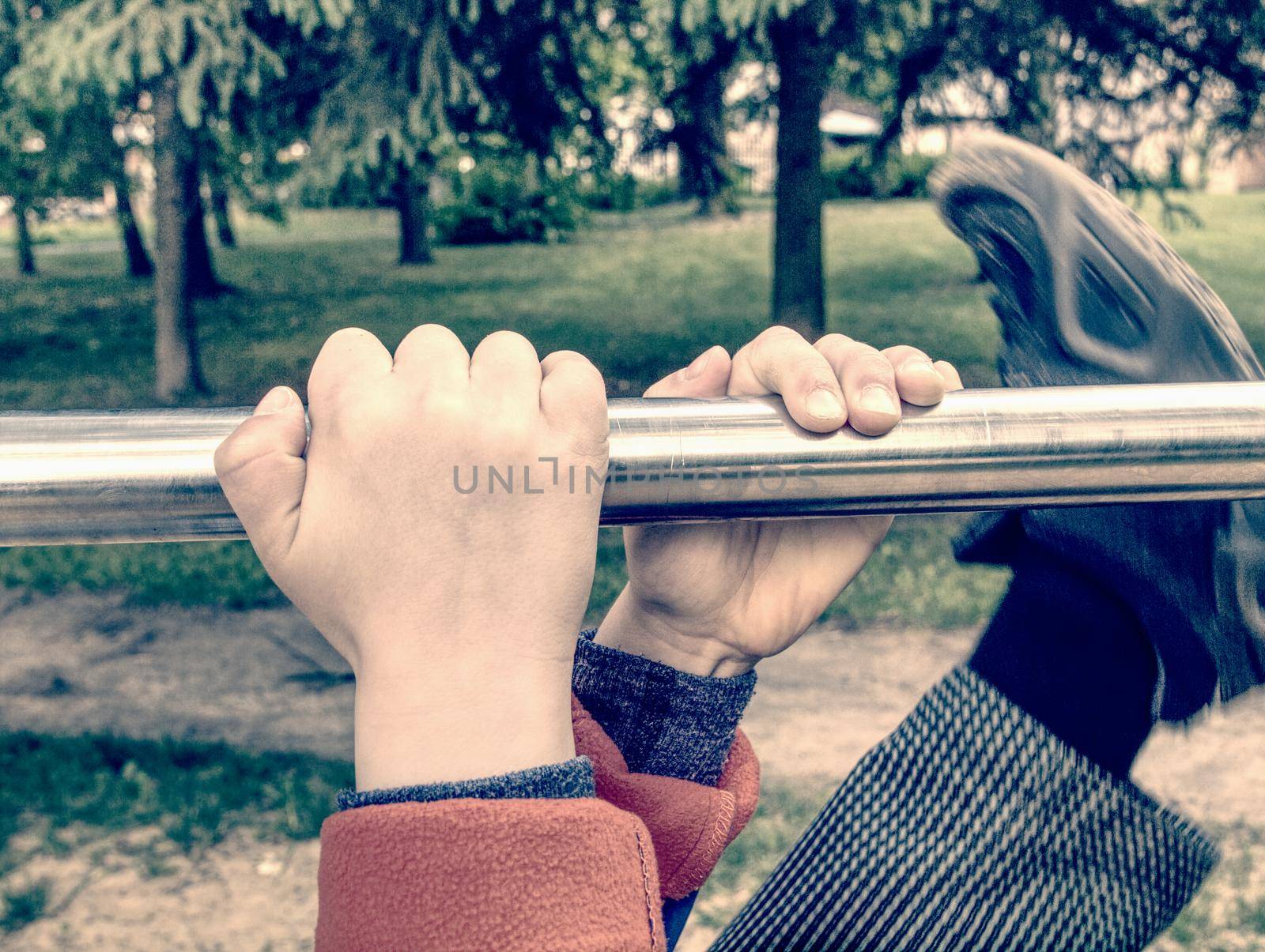 Young boy hang on stainless bar by his hand to exercise at outdoor playground  