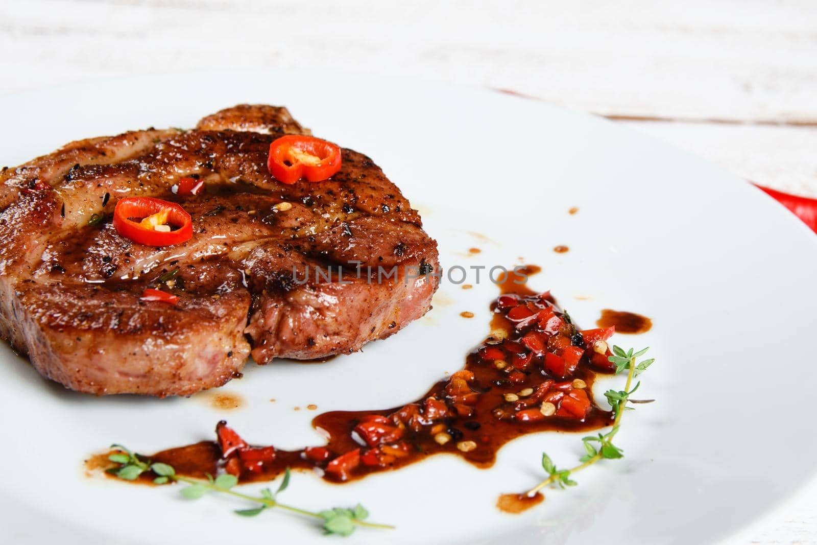 Steak on a white plate with spicy red sauce. Stock image.