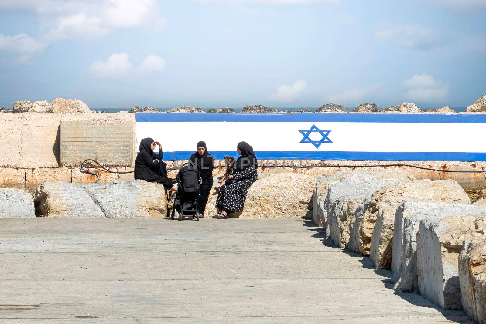 Arab women with Chador, sitting in the port of Old Jaffa with the Israeli flag in the background. The concept for peace. High quality photo