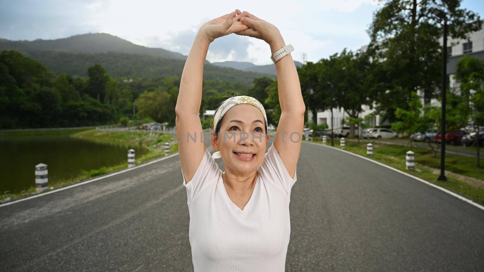 Smiling middle aged woman stretching muscle before workout session at the park in early morning. Healthy lifestyle, fitness and sport concept concept.