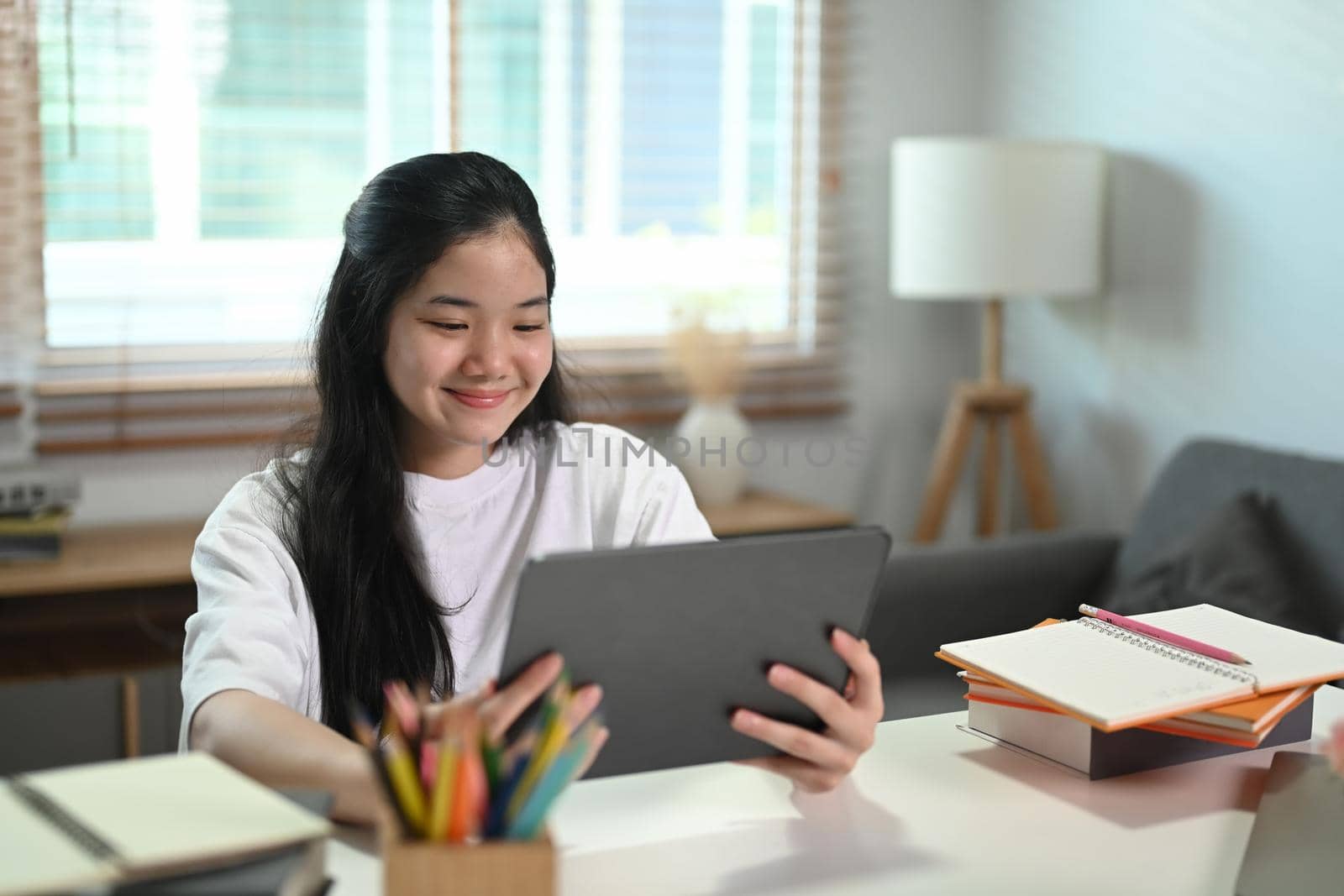 Smiling asian girl learning online in virtual classroom on digital tablet at home.