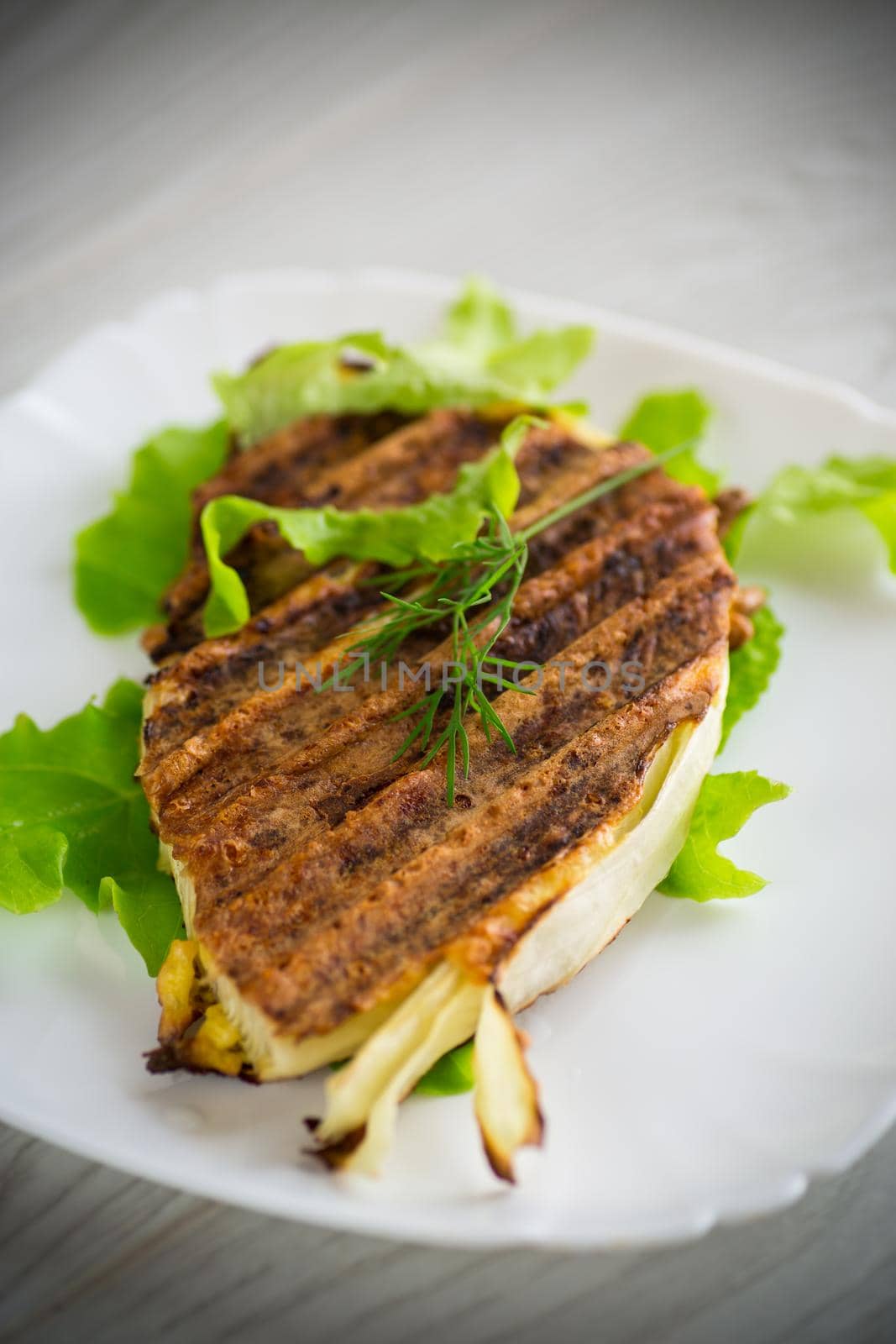 piece of grilled baked cabbage with spices in a plate, on a wooden table.