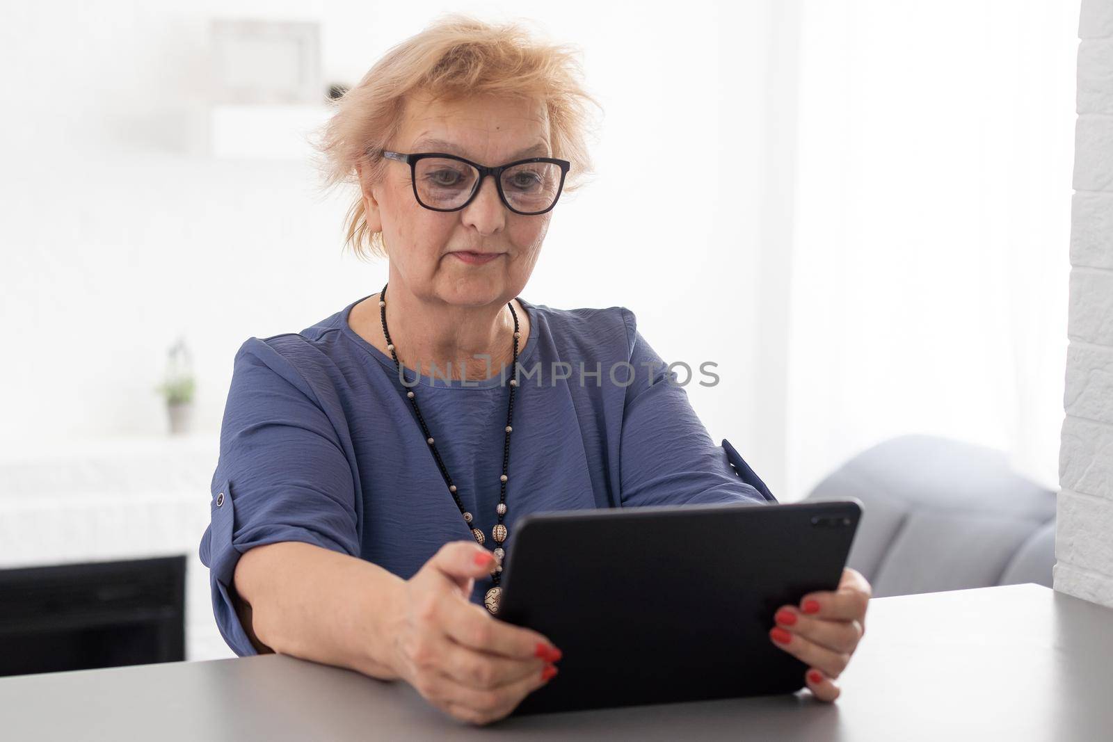 Authentic shot of a happy grandmother is making a video call to relatives with a laptop at home. Concept of technology, modern generation,family, connection, authenticity.