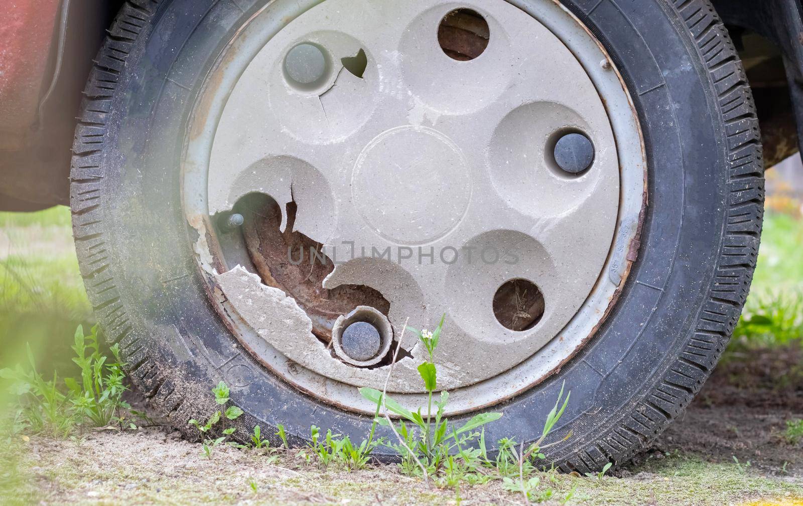 Weathered car wheel with dirt and grime. Rusty abandoned car in the parking lot. Restoration of a retro car. Flat tire. Vintage wheel with classic red car cap