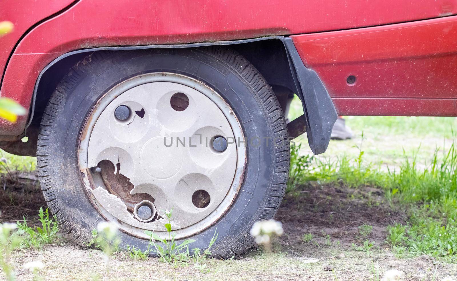 Weathered car wheel with dirt and grime. Rusty abandoned car in the parking lot. Restoration of a retro car. Flat tire. Vintage wheel with classic red car cap
