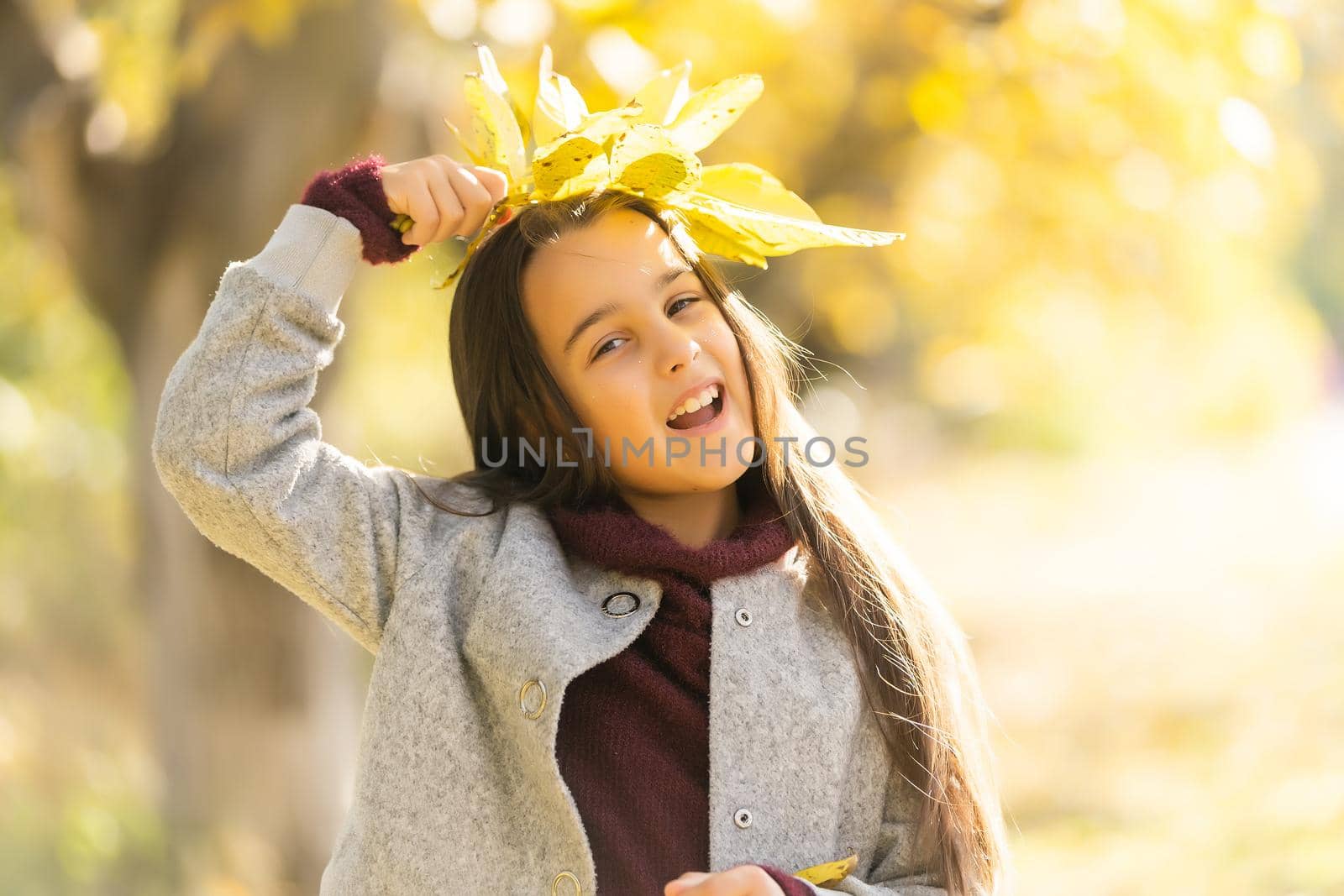 Little girl in a coat at autumn holding leaves.