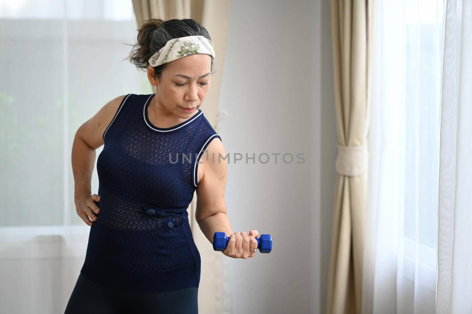 Sporty mature woman doing her workout routine, exercising with dumbbells at home. Healthy lifestyle and sport concept.