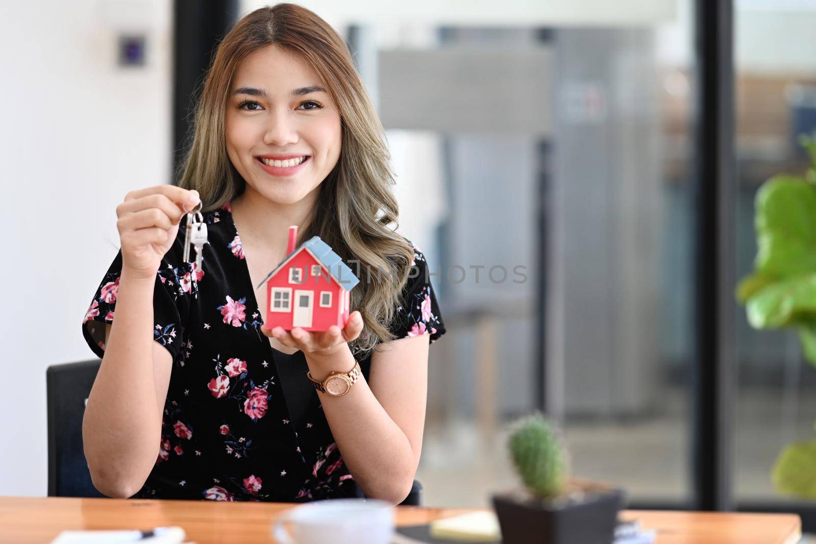Beautiful asian woman holding house model and house key in hand. Insurance or loan real estate concept.