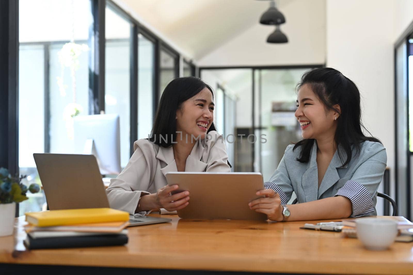 Two young businesswomen using digital tablet and discussing on new startup project together. by prathanchorruangsak