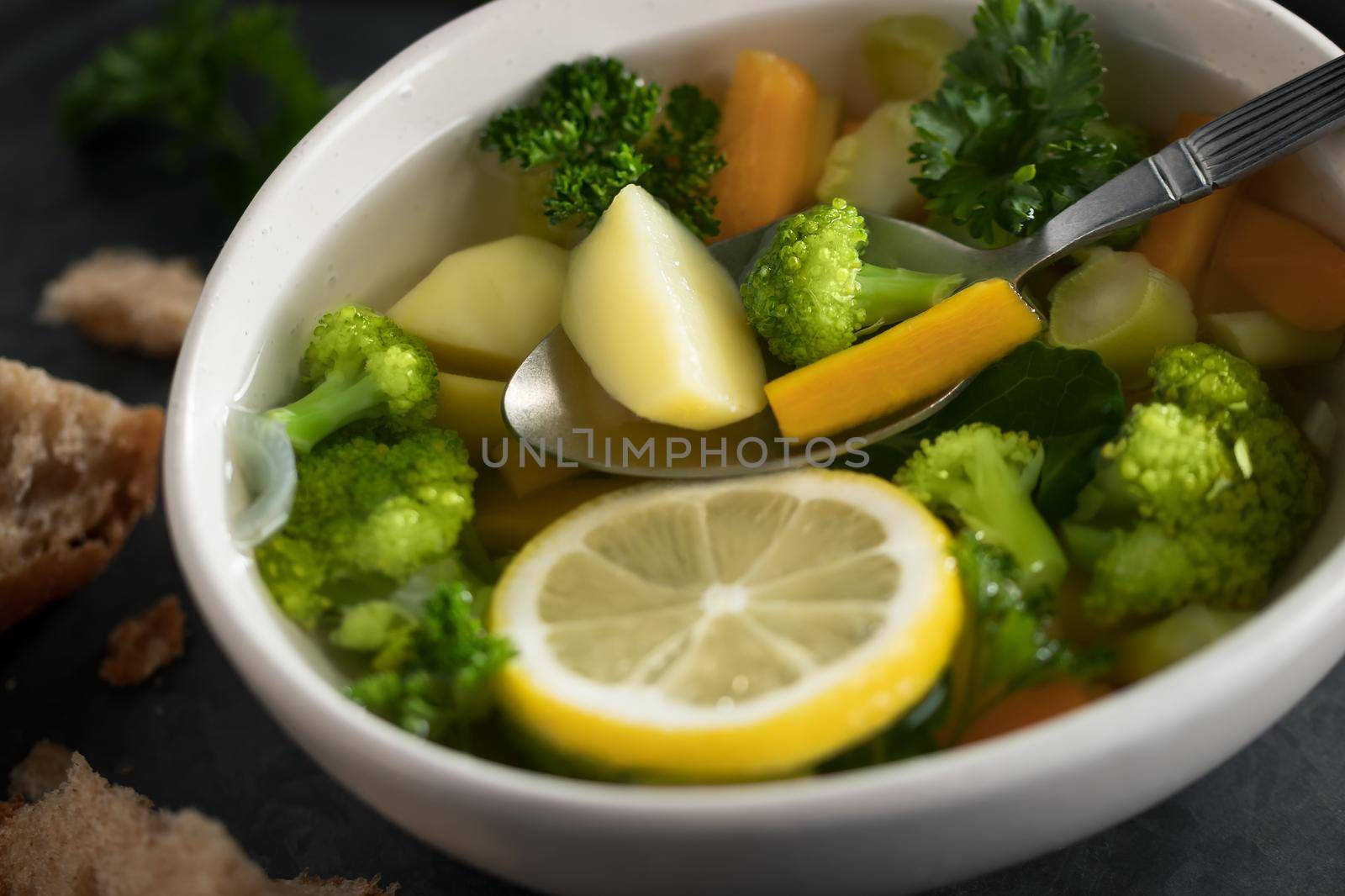 Vegetarian vegetable soup with carrots, broccoli and parsley in a light bowl on a metal tray on a wooden table.