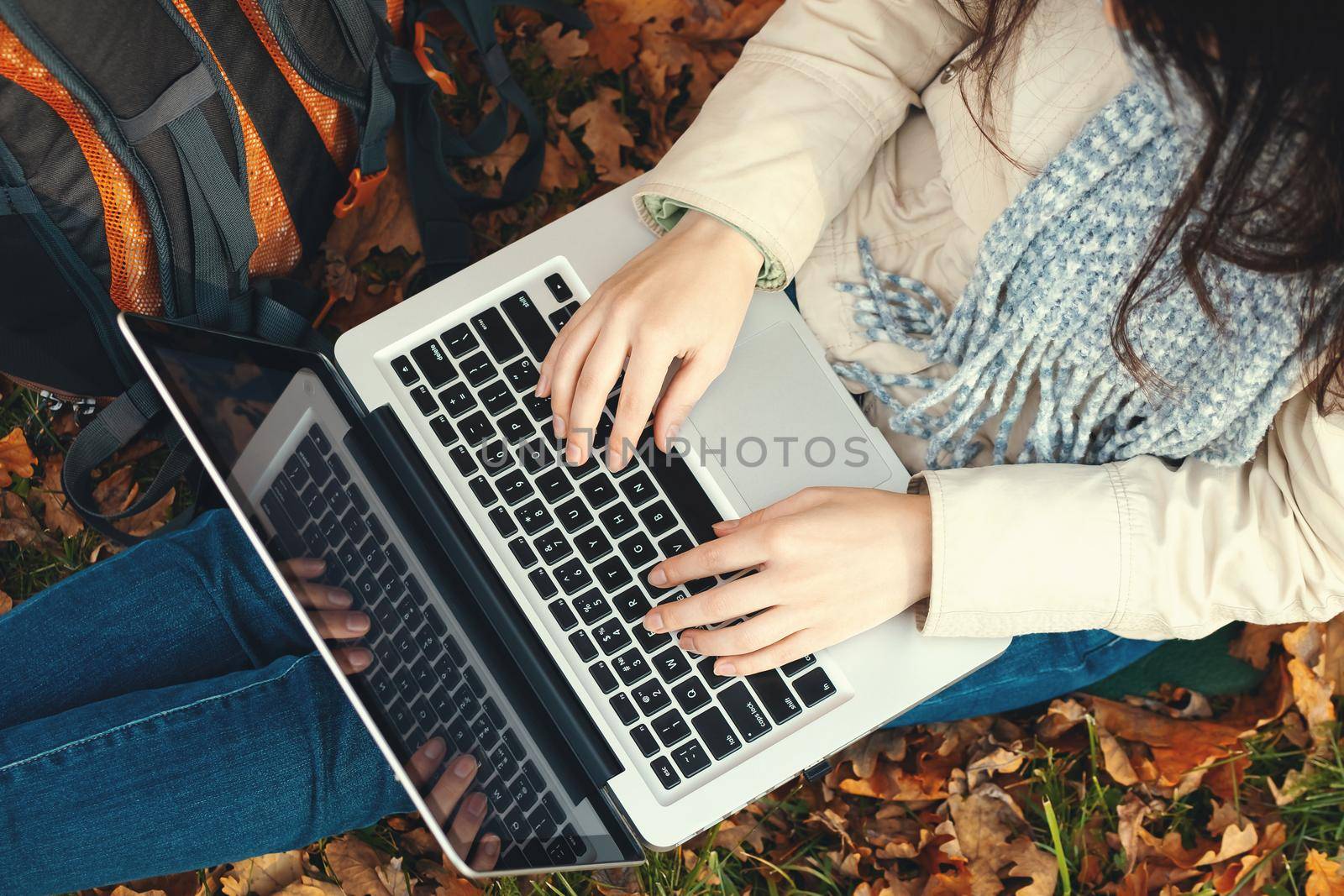 girl uses a laptop while sitting on the grass in the autumn park by galsand