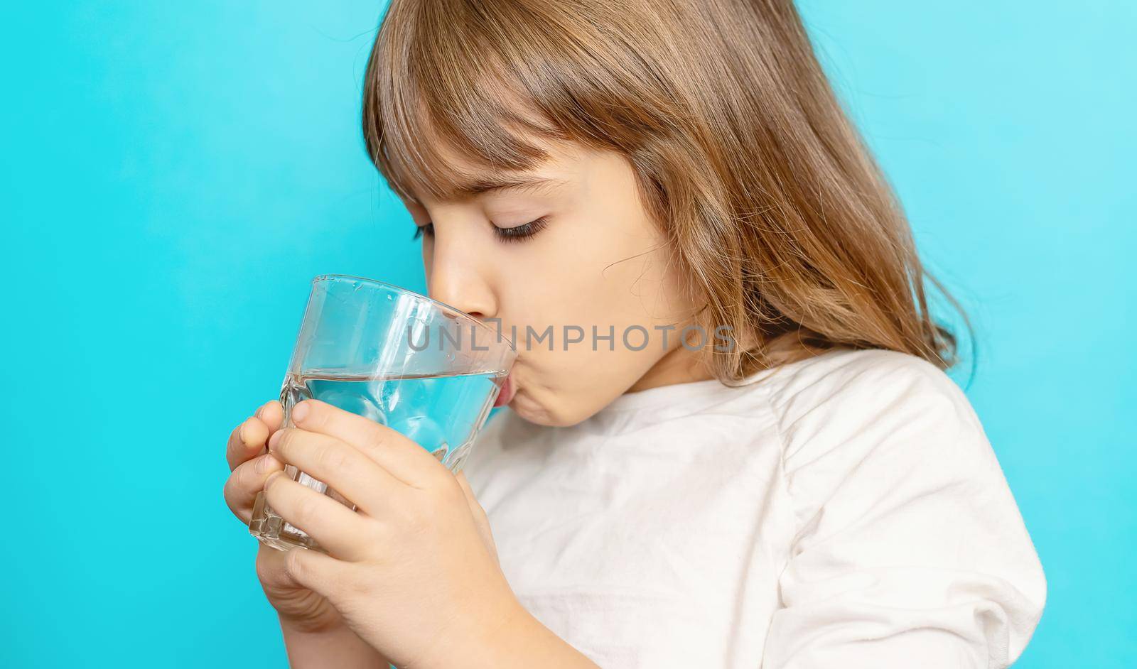 Child girl drinks water from a glass. Selective focus. by yanadjana