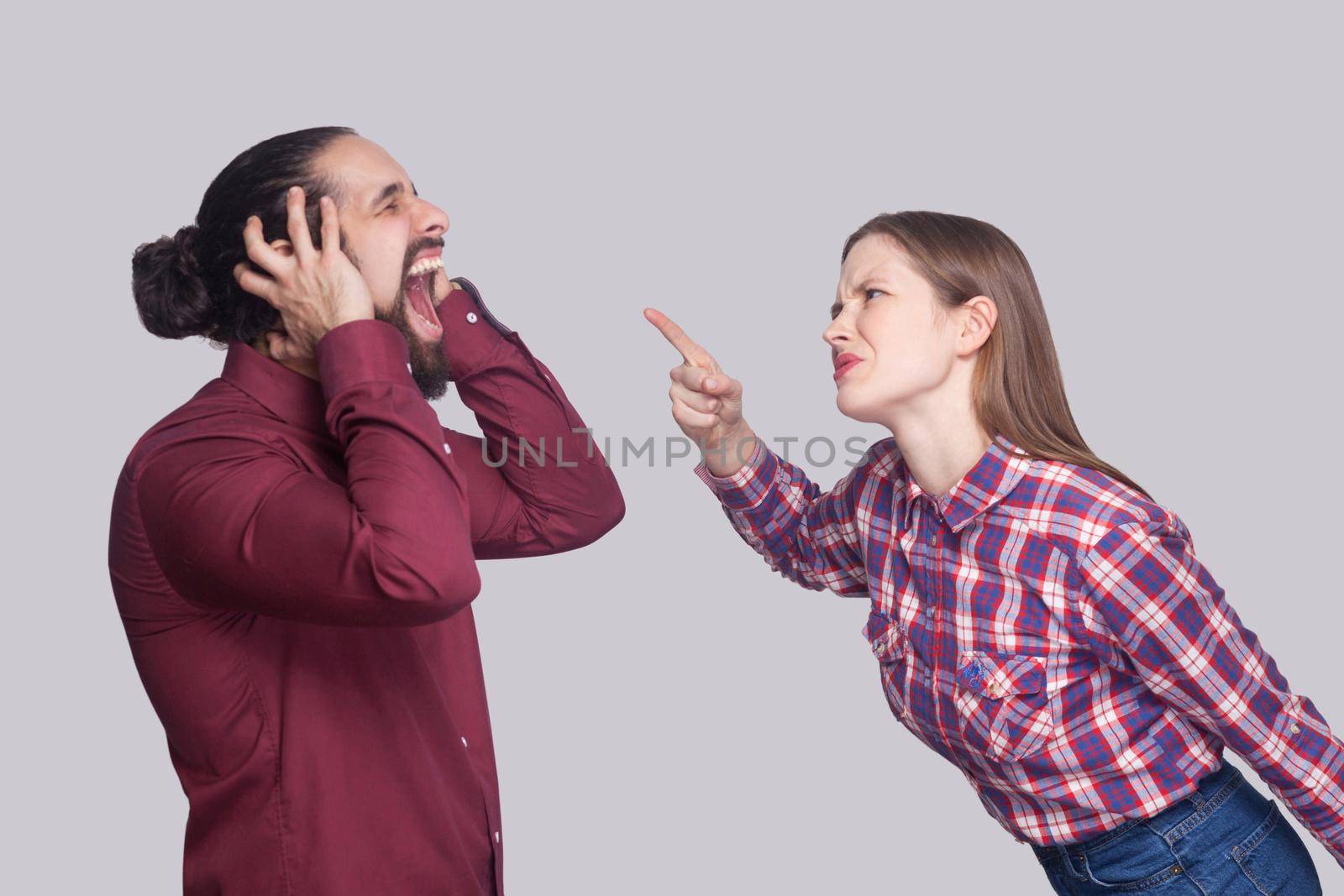 Profile side view portrait of angry woman standing and blaming at screaming unhappy man with black collected hair. indoor studio shot, isolated on gray background.
