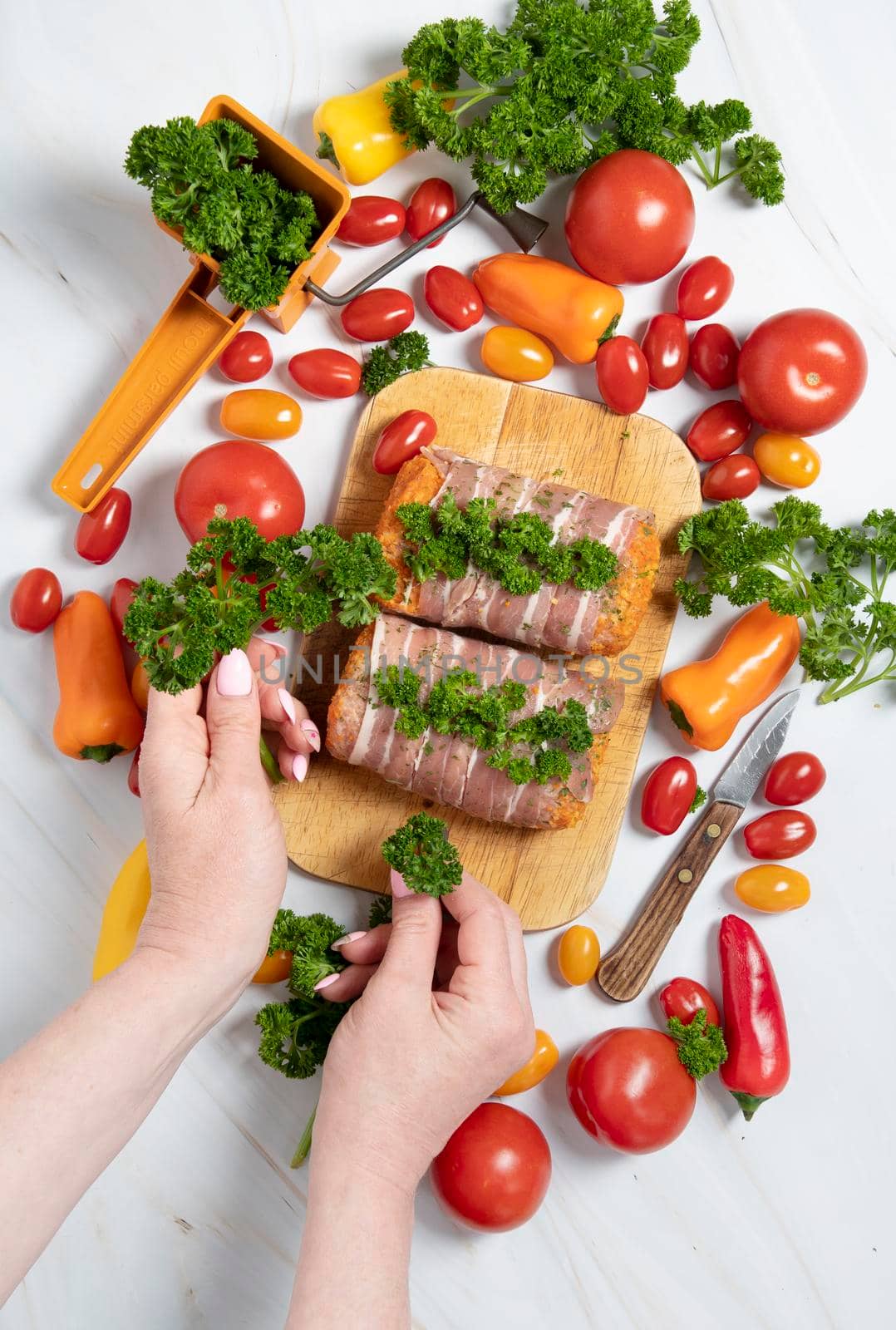 female hands decorate with parsley minced meat sausages in bacon with fresh vegetables, cherry tomatoes, sweet peppers, colorful food flat lay. High quality photo