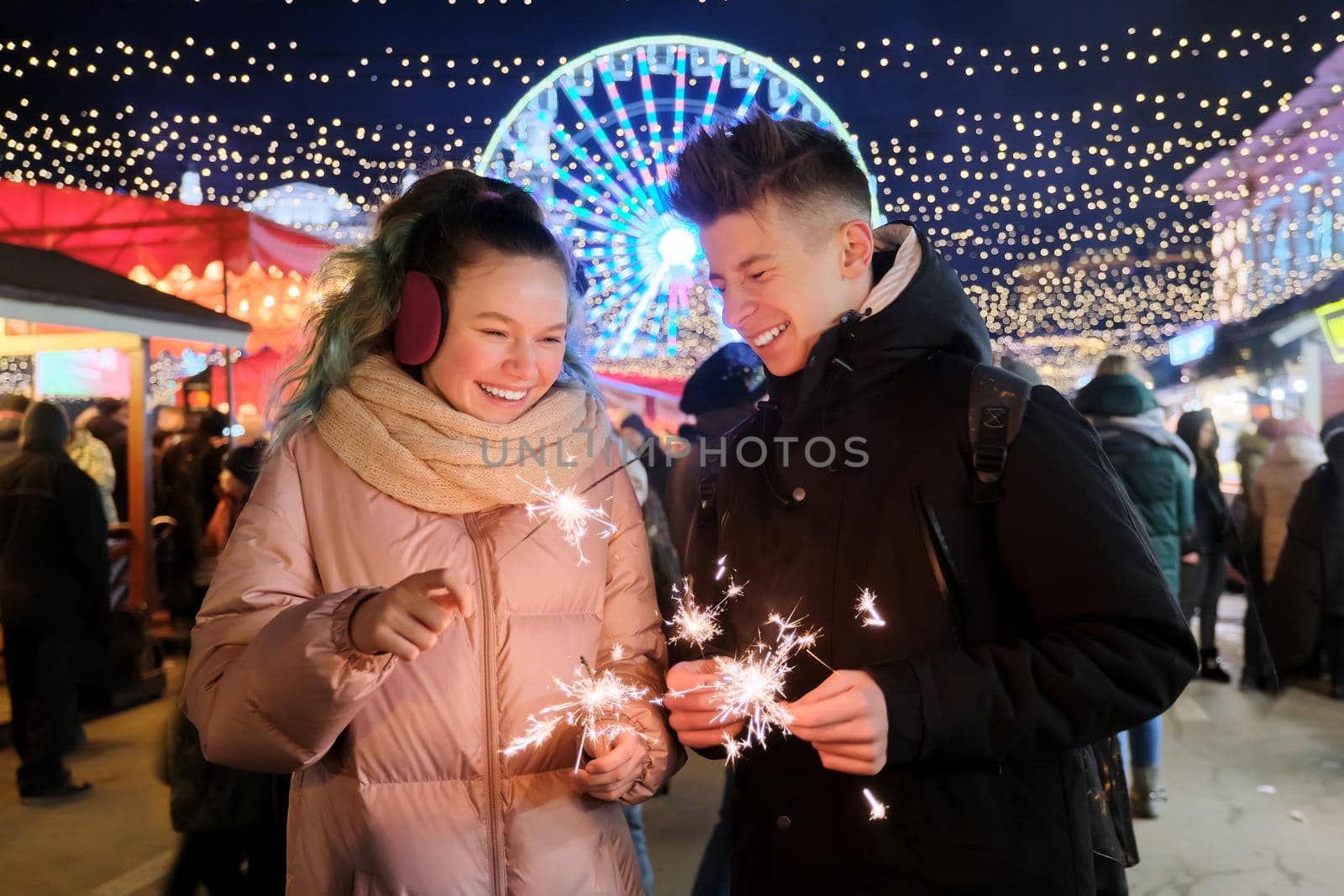 Happy teenage couple with sparklers celebrating and having fun at Christmas market by VH-studio