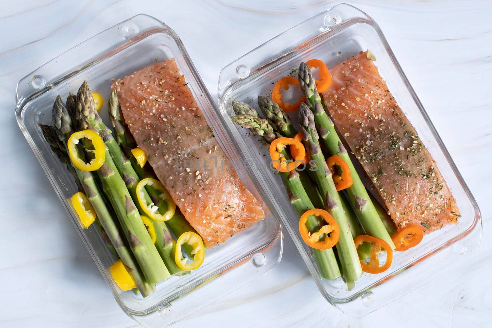 raw red salmon with salt and spices with green asparagus and paprika in a baking dish covered with foil. High quality photo