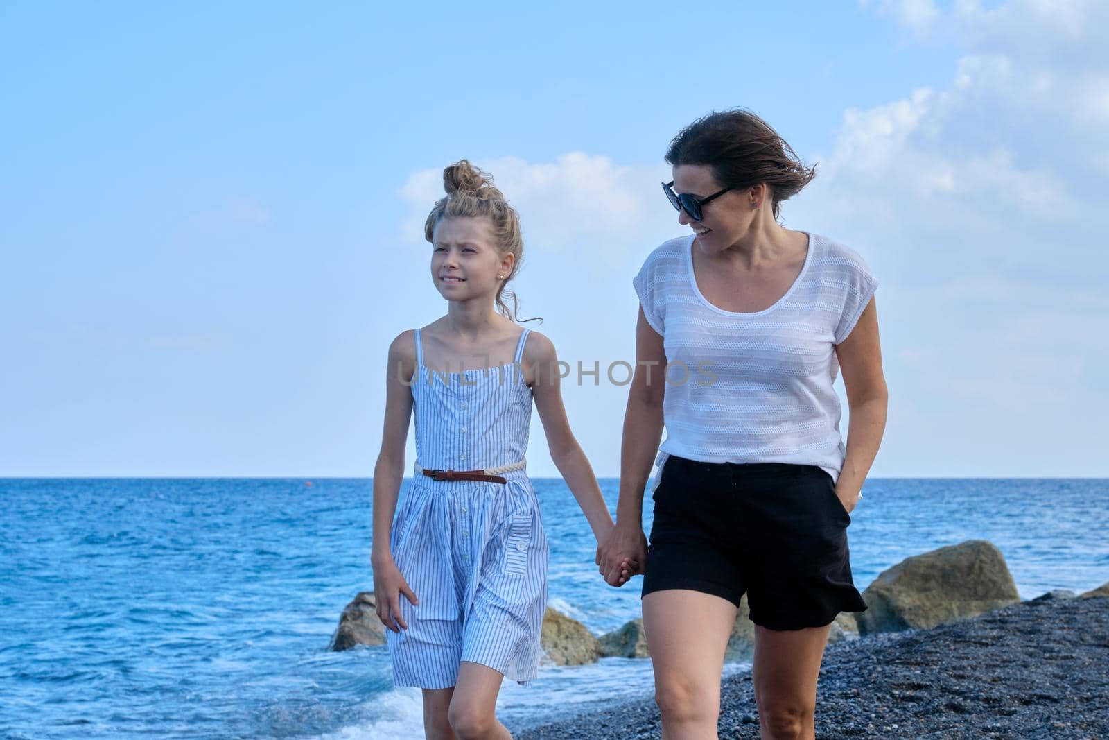Happy mother and daughter kid walking together holding hands along sea beach by VH-studio